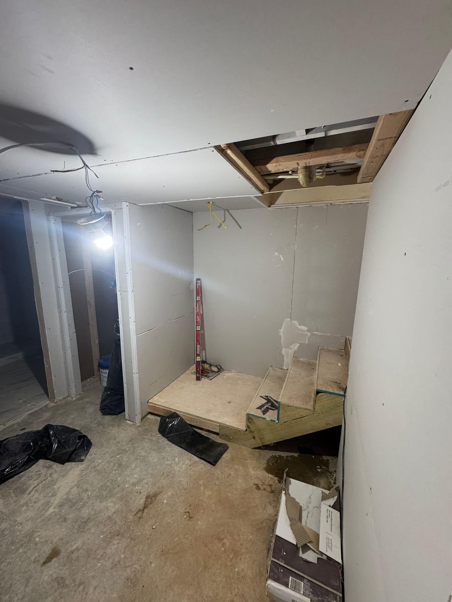 Interior renovation: Damaged ceiling, unfinished walls, and stairwell in a room. Construction tools visible.
