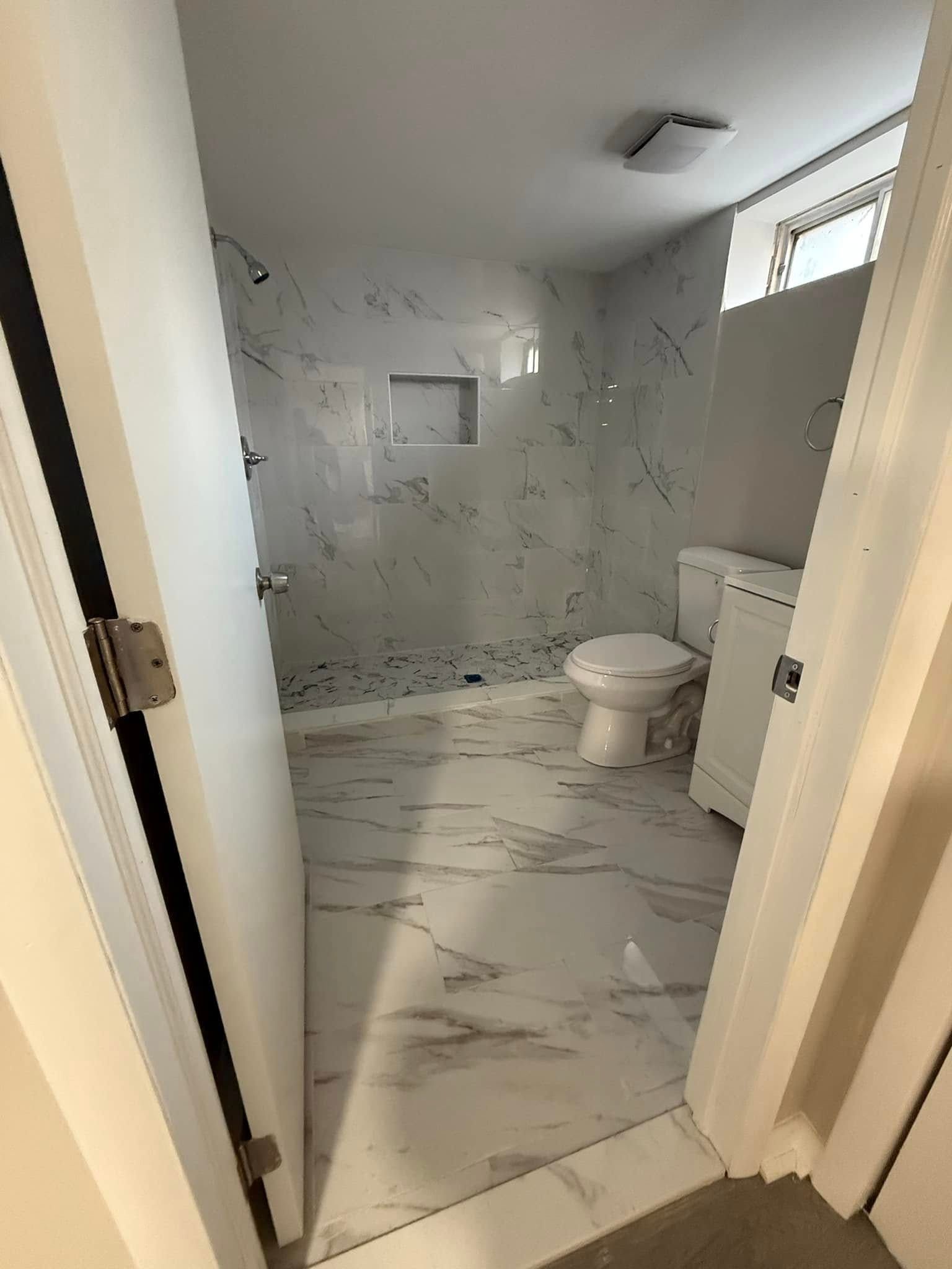 Bathroom with marble-like tile. Toilet, shower, and a niche are visible through an open door.