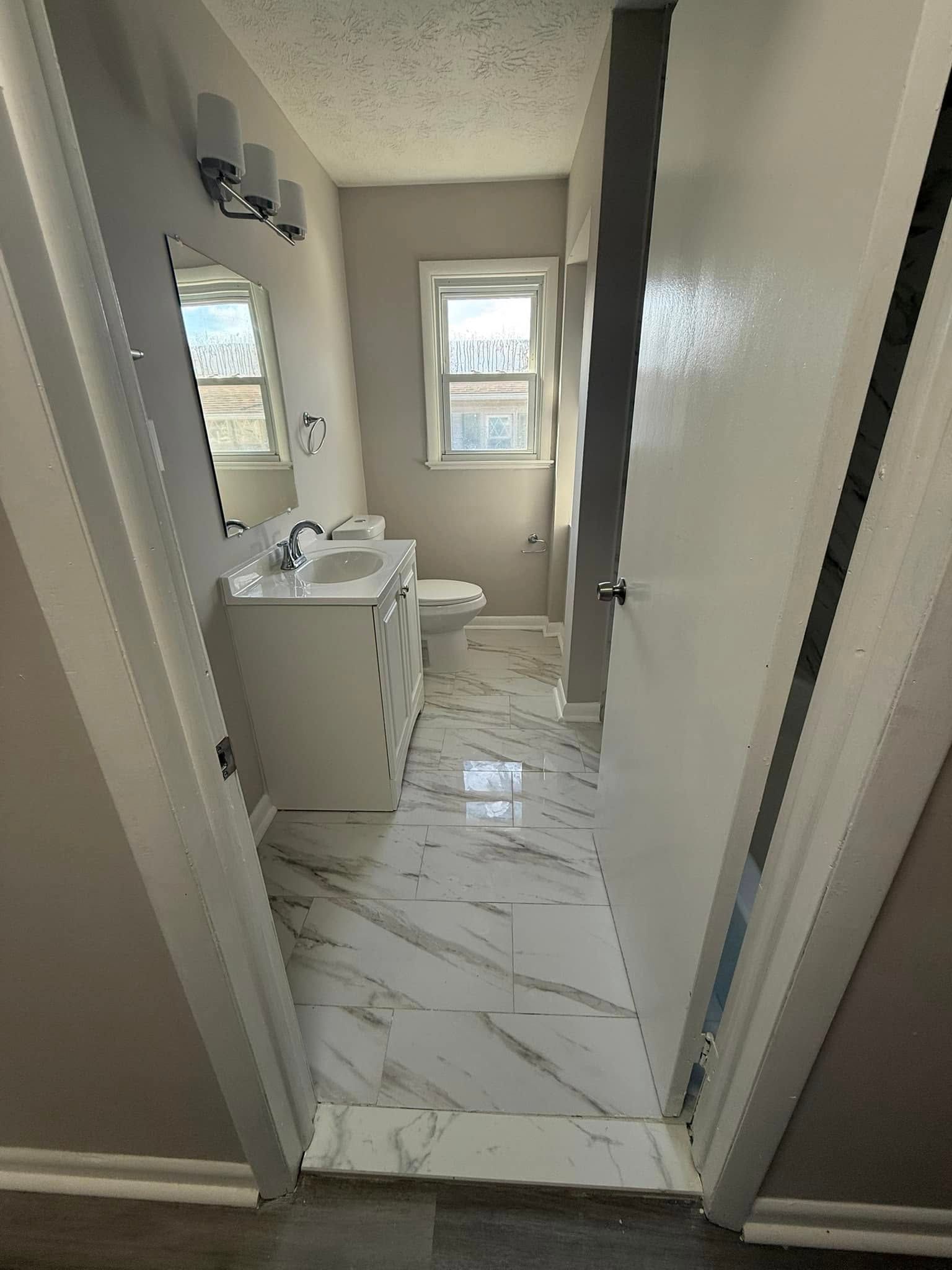 Bathroom with white vanity, toilet, and marble-like floor. Window provides natural light.
