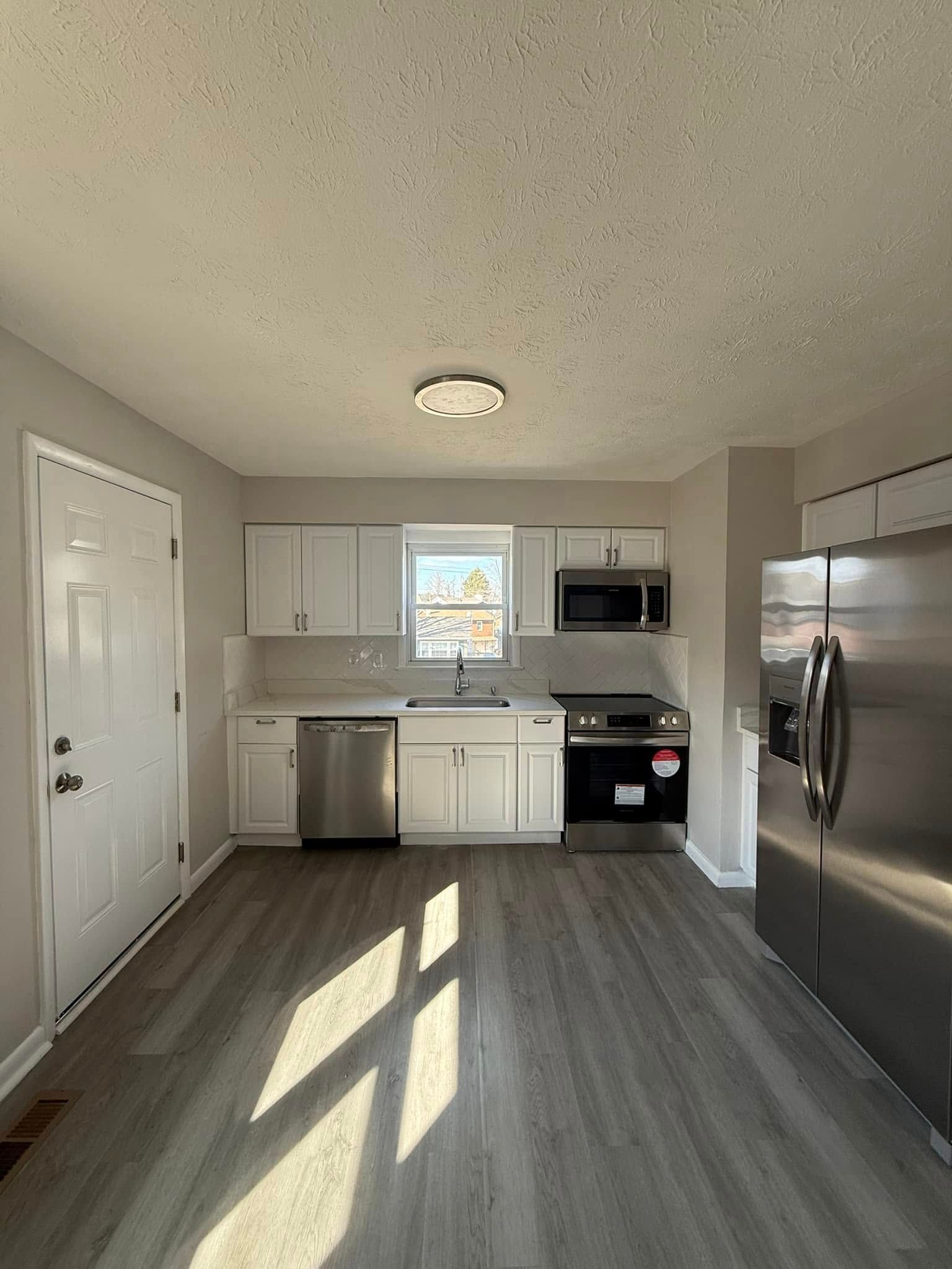 Bright kitchen with white cabinets, stainless steel appliances, and gray flooring.