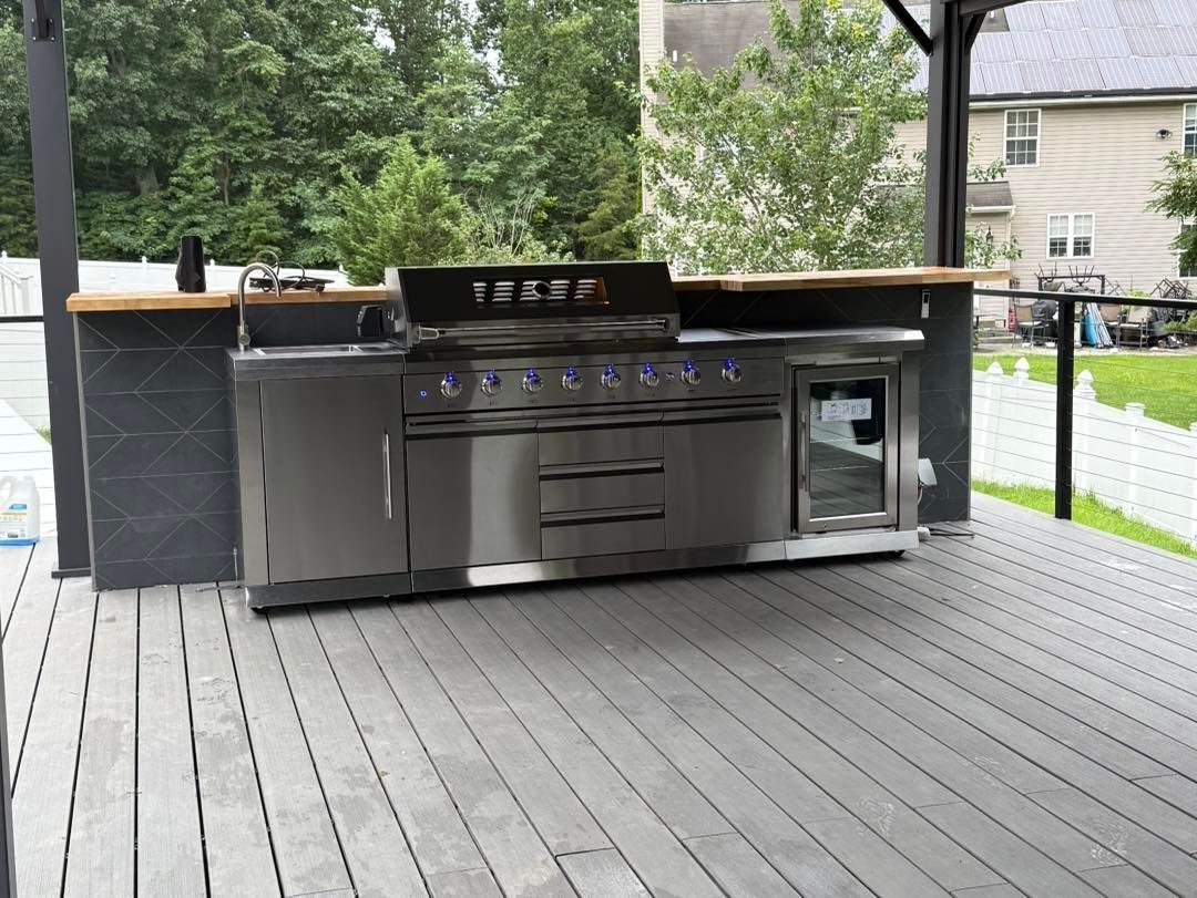 Outdoor kitchen with stainless steel grill, sink, and mini fridge on a gray deck.