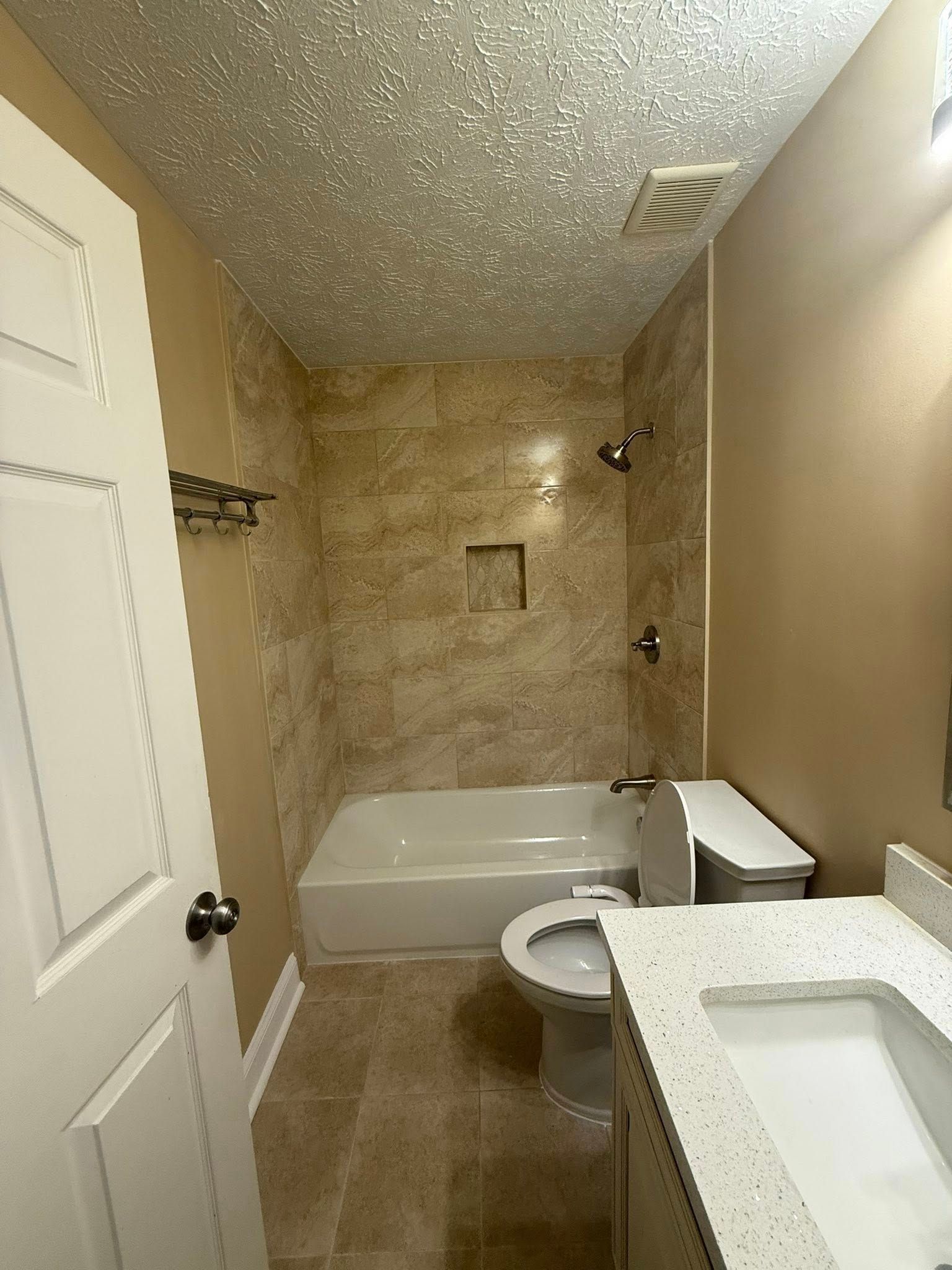 Bathroom with tan tile, white tub, toilet, and vanity. Glittered ceiling, silver fixtures.