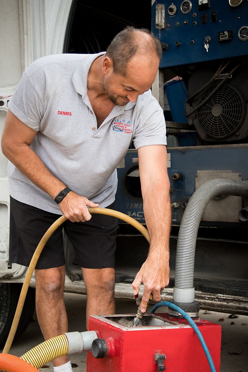Man in gray shirt connecting hoses to a red machine, outdoors.