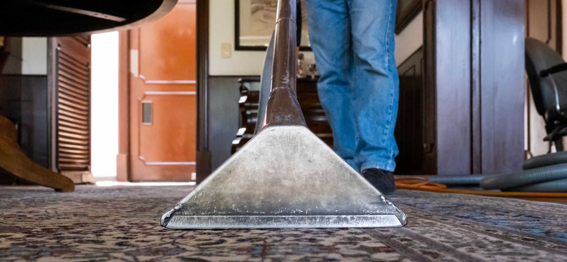 Man vacuuming a red patterned rug in a living room with a white couch and curtains. Man vacuuming a red patterned rug in a living room with a white couch and curtains.