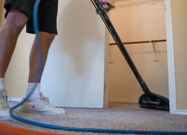 Person vacuuming carpet inside a closet; blue hose and black vacuum head. Person vacuuming carpet inside a closet; blue hose and black vacuum head.