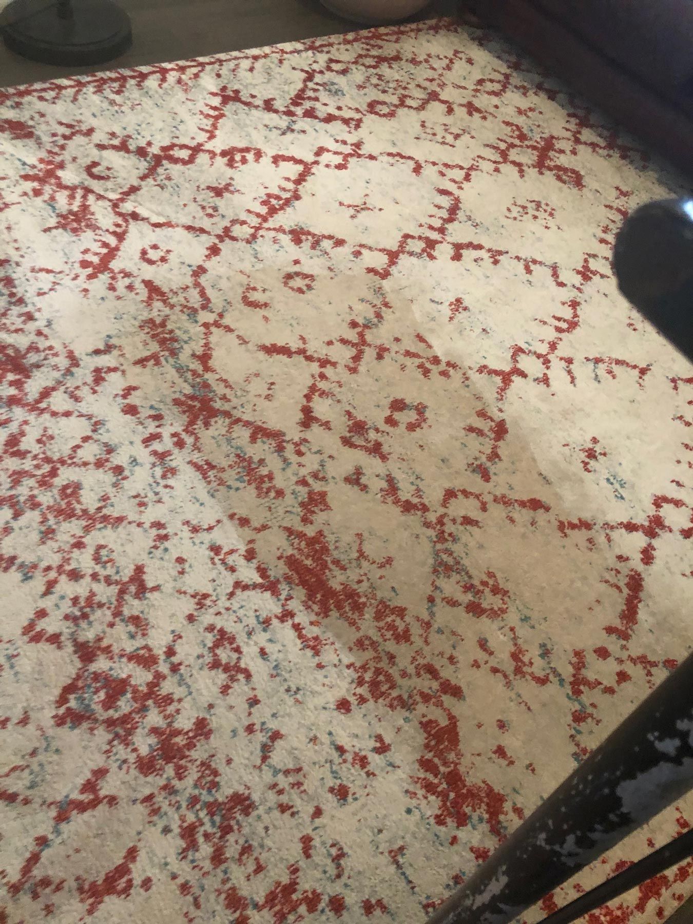 Beige rug with red geometric pattern on a wooden floor.