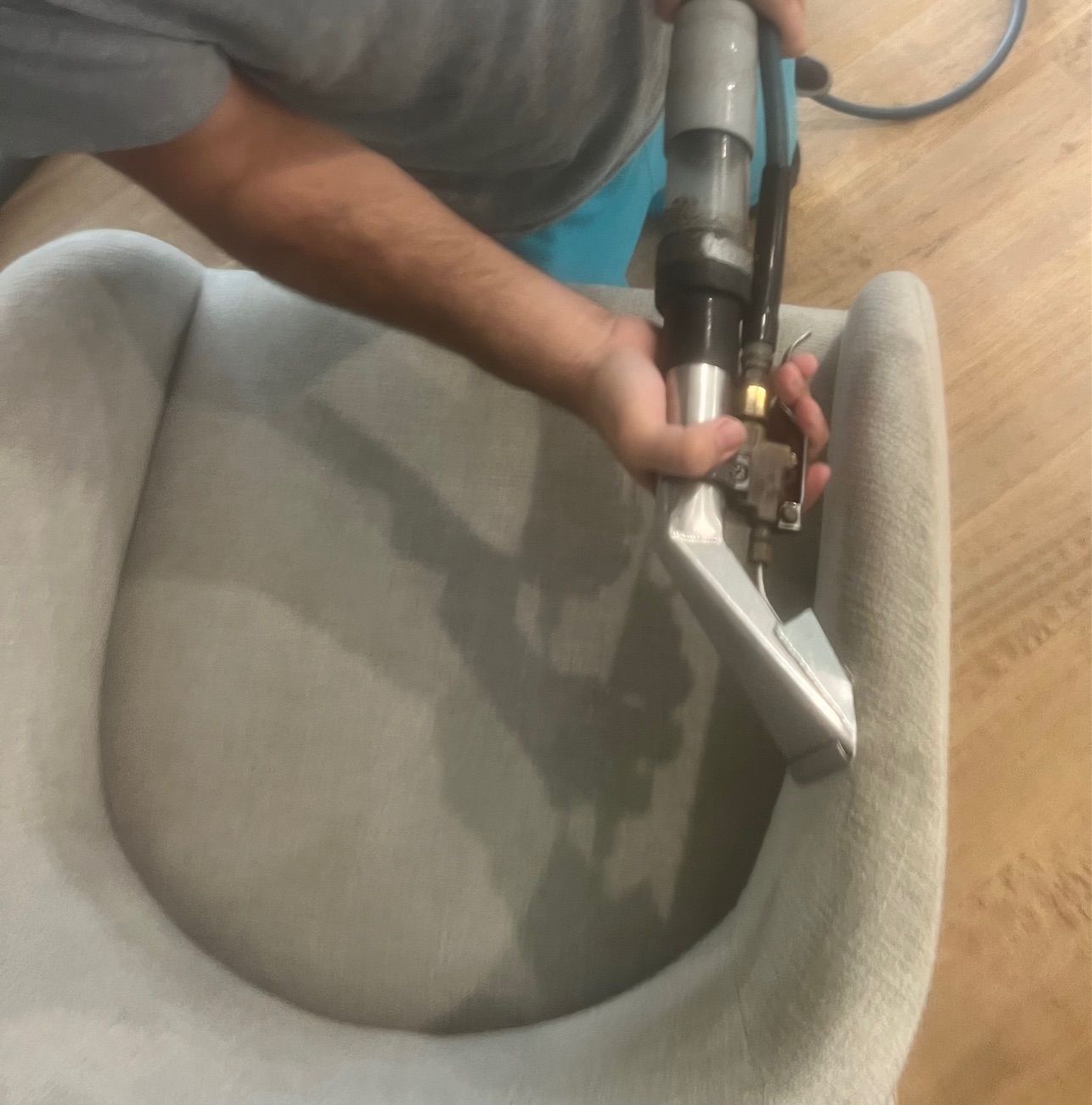 Person with yellow gloves scrubbing a patterned rug with a brush, sponge nearby. Person cleaning a light gray armchair with a steam cleaner.