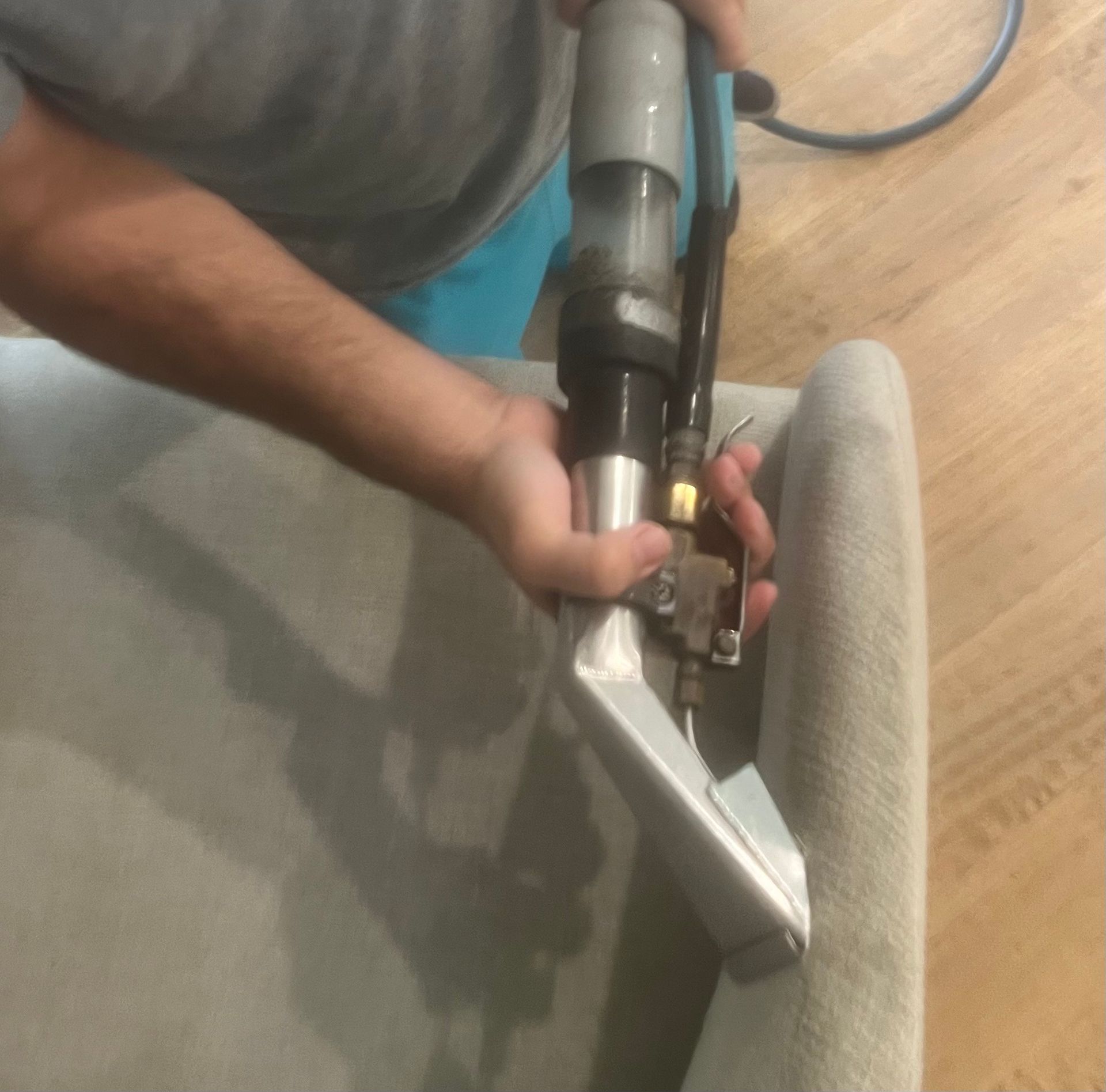 Person in black gloves cleaning a gray couch with a cleaning machine.