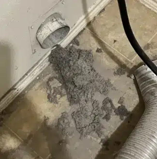 Dryer vent with a large pile of lint on a wet, light-colored floor. Dryer vent with a large pile of lint on a wet, light-colored floor.