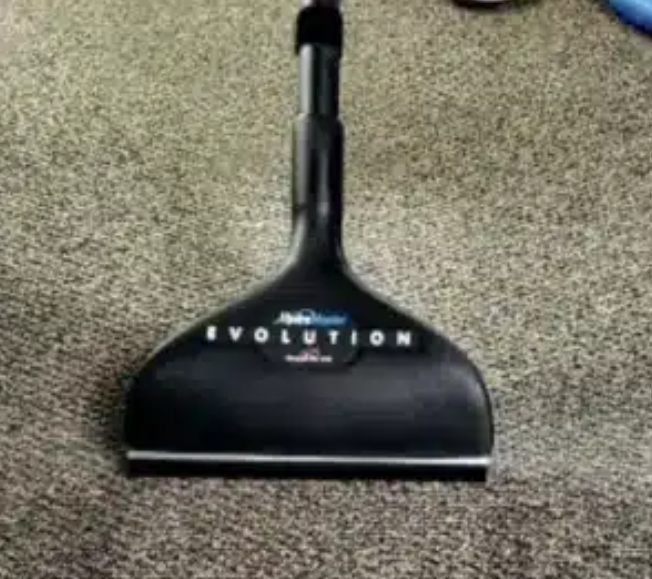 Person cleaning gray carpet with a carpet cleaner; cleaning progress visible. Person cleaning gray carpet with a carpet cleaner; cleaning progress visible.