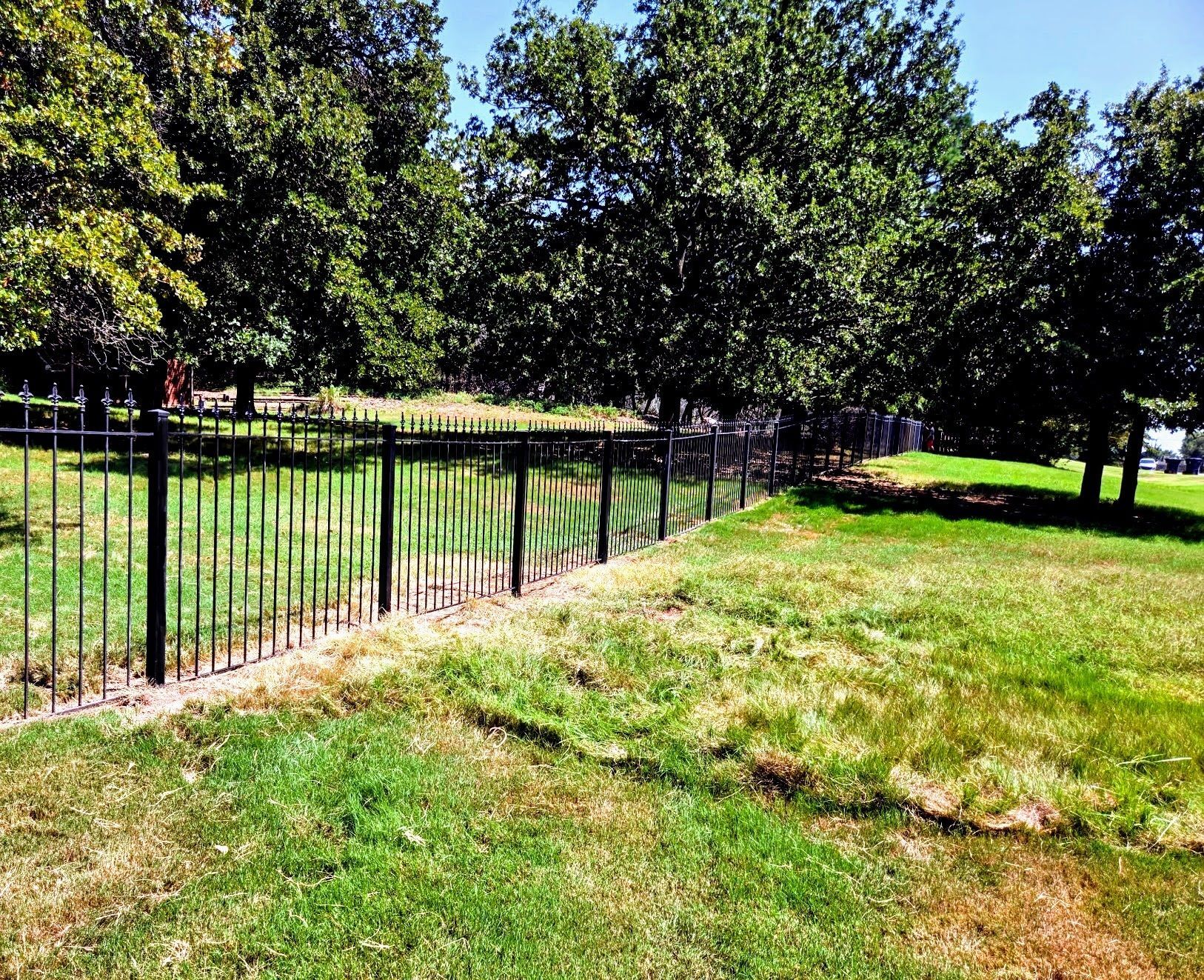 Wooden fence with a small, round window at the bottom, in front of a house and green grass.