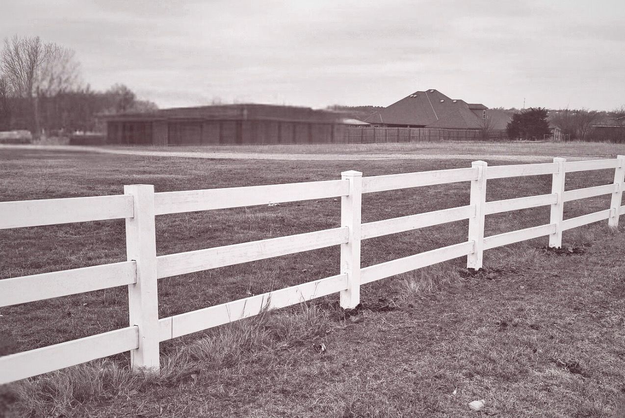 A black and white photo of a white fence in a field.