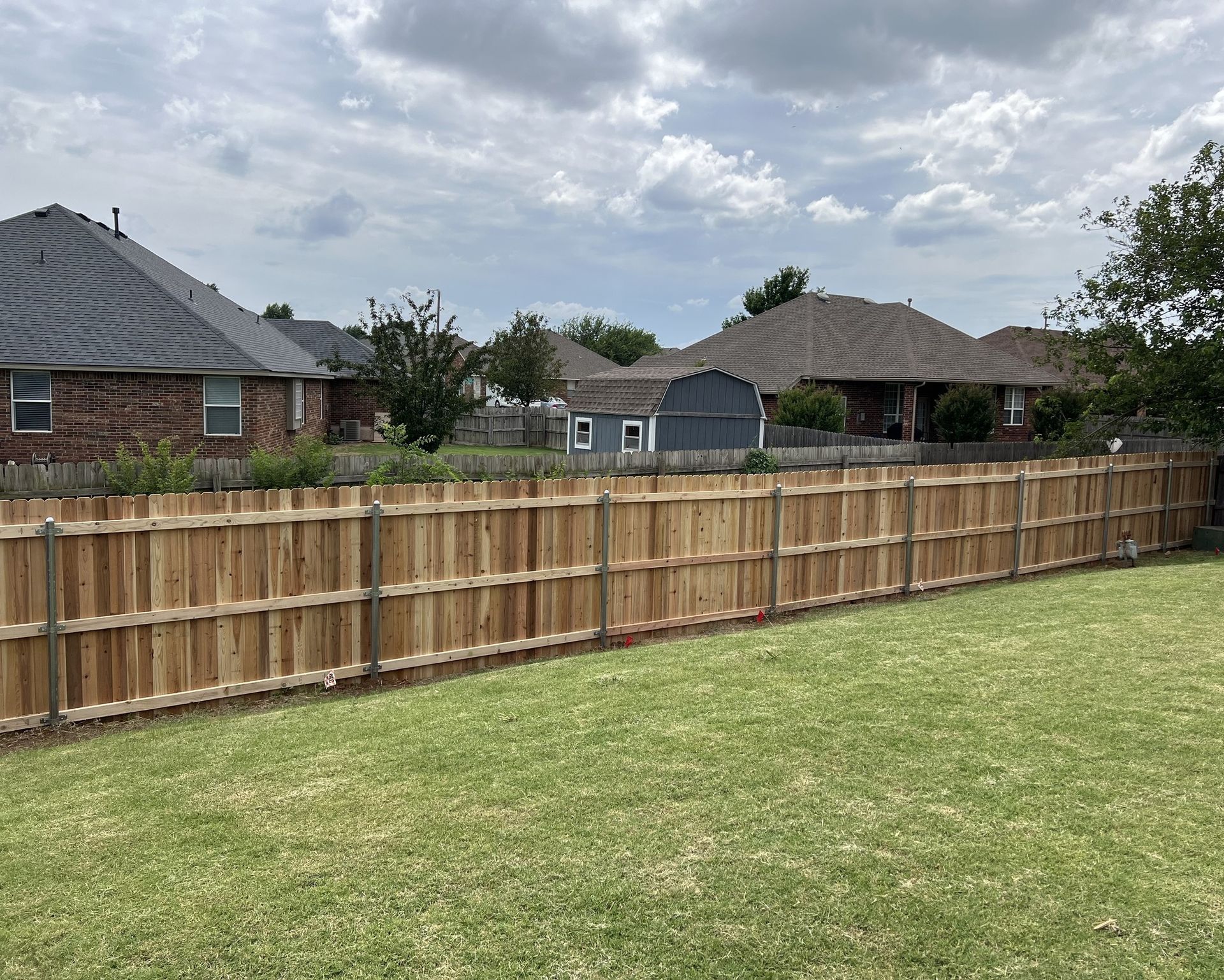 A wooden fence surrounds a lush green yard with houses in the background.