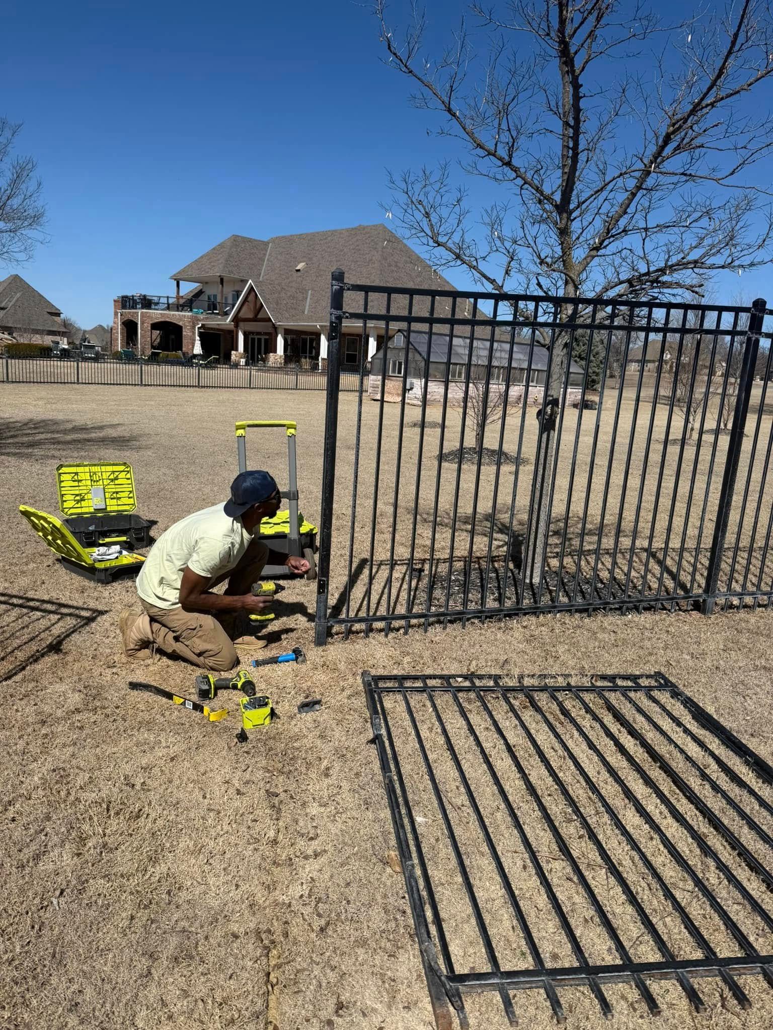 A man is installing a metal fence in a backyard.