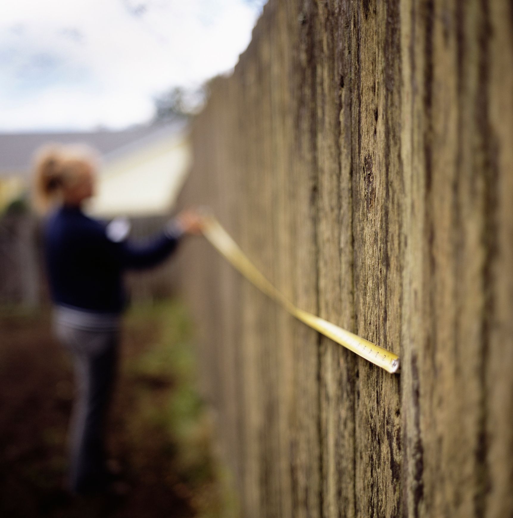 A man is measuring a wooden fence with a tape measure.