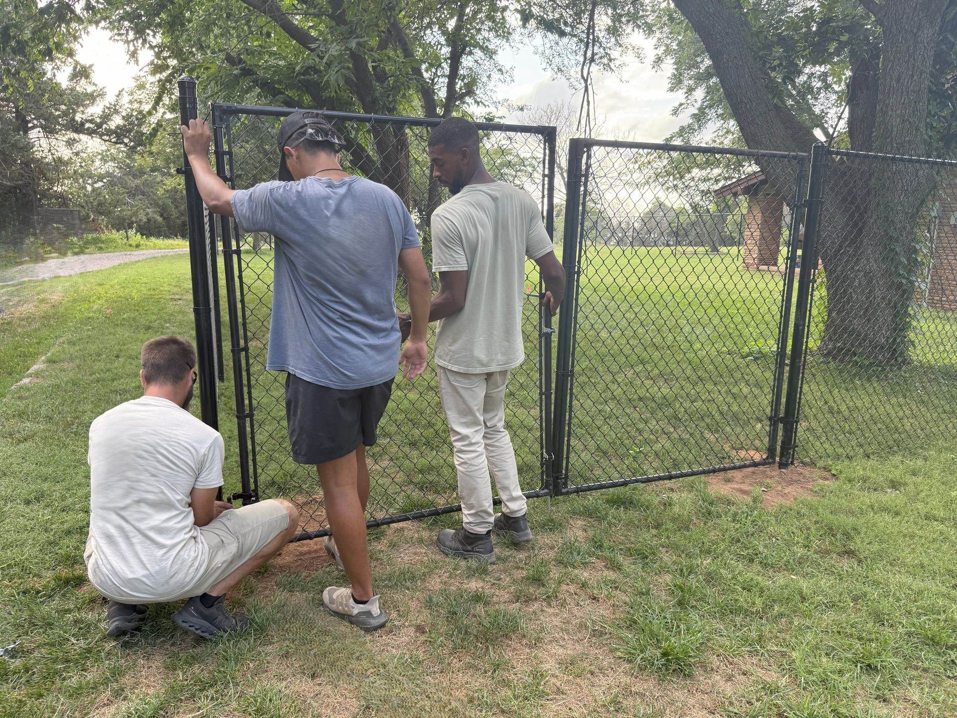 Fencing workers installing a chain-link gate on a fence outside.