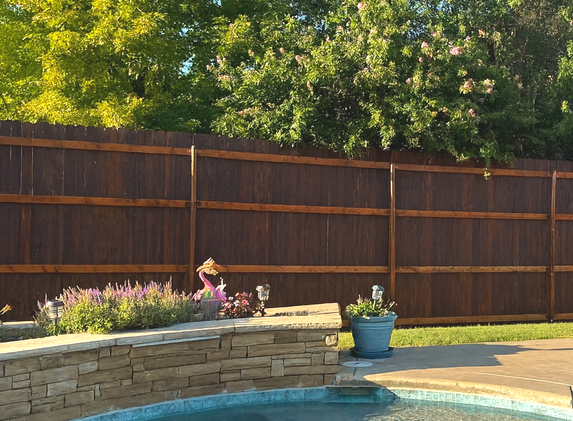 Wooden privacy fence, pool, and garden with flowers.