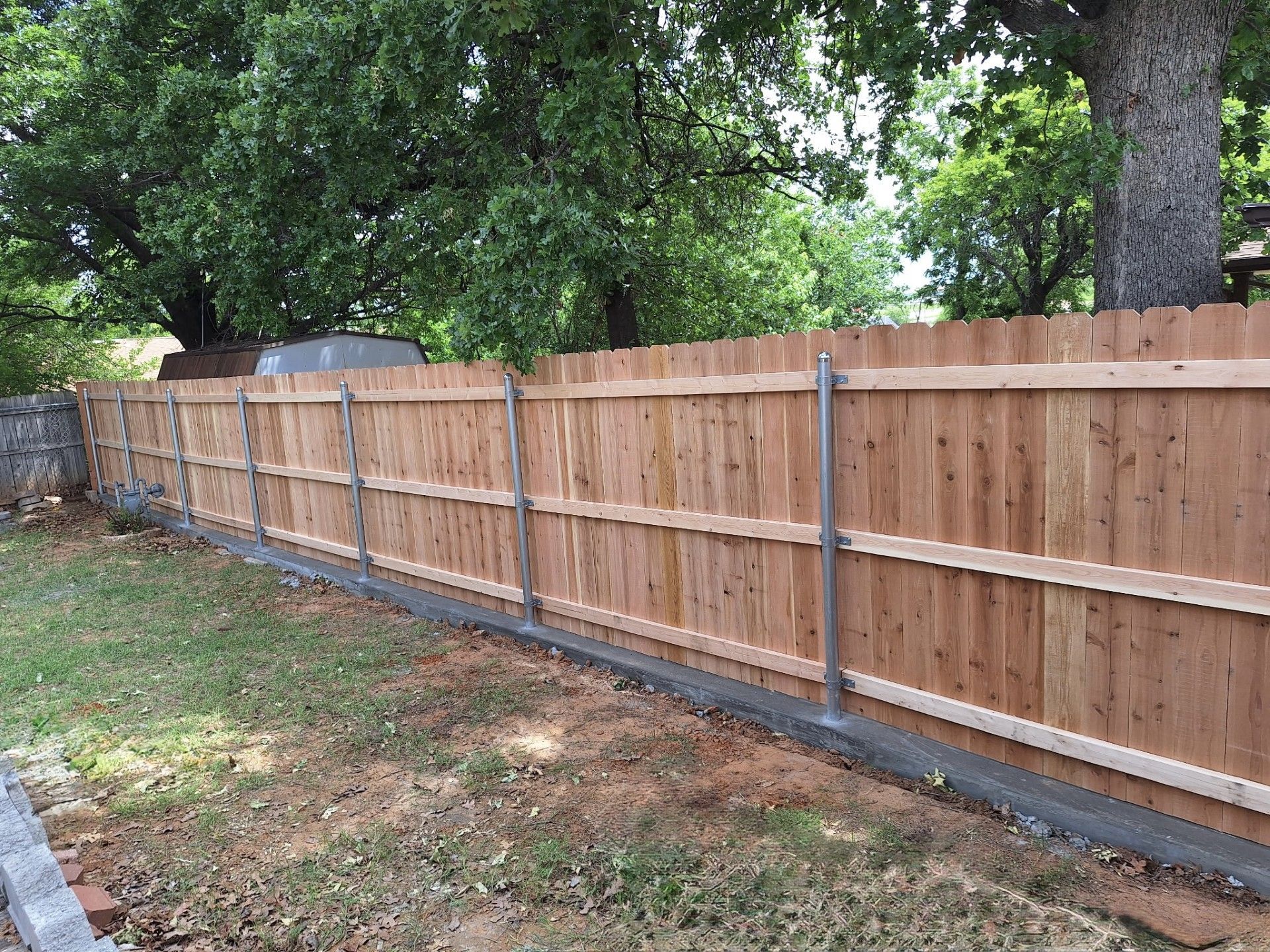A wooden fence is being built in a backyard with trees in the background.