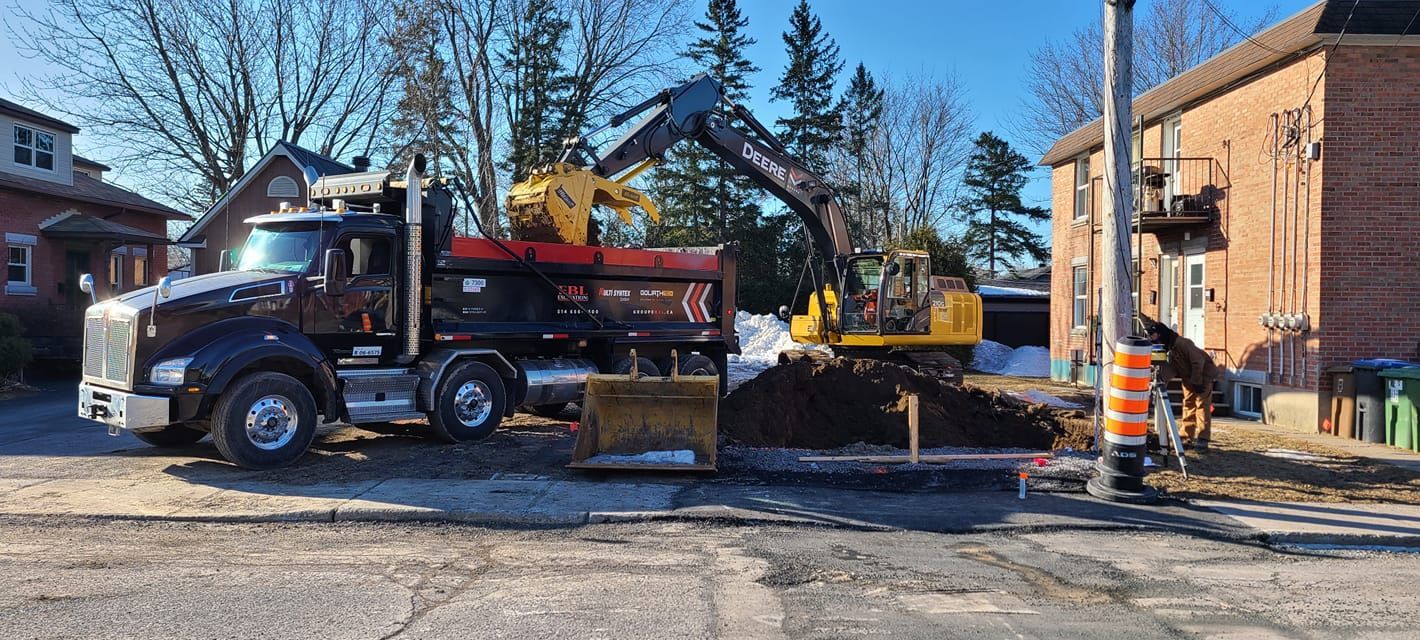 Un camion à benne basculante auquel est attaché un bulldozer est garé devant un bâtiment.