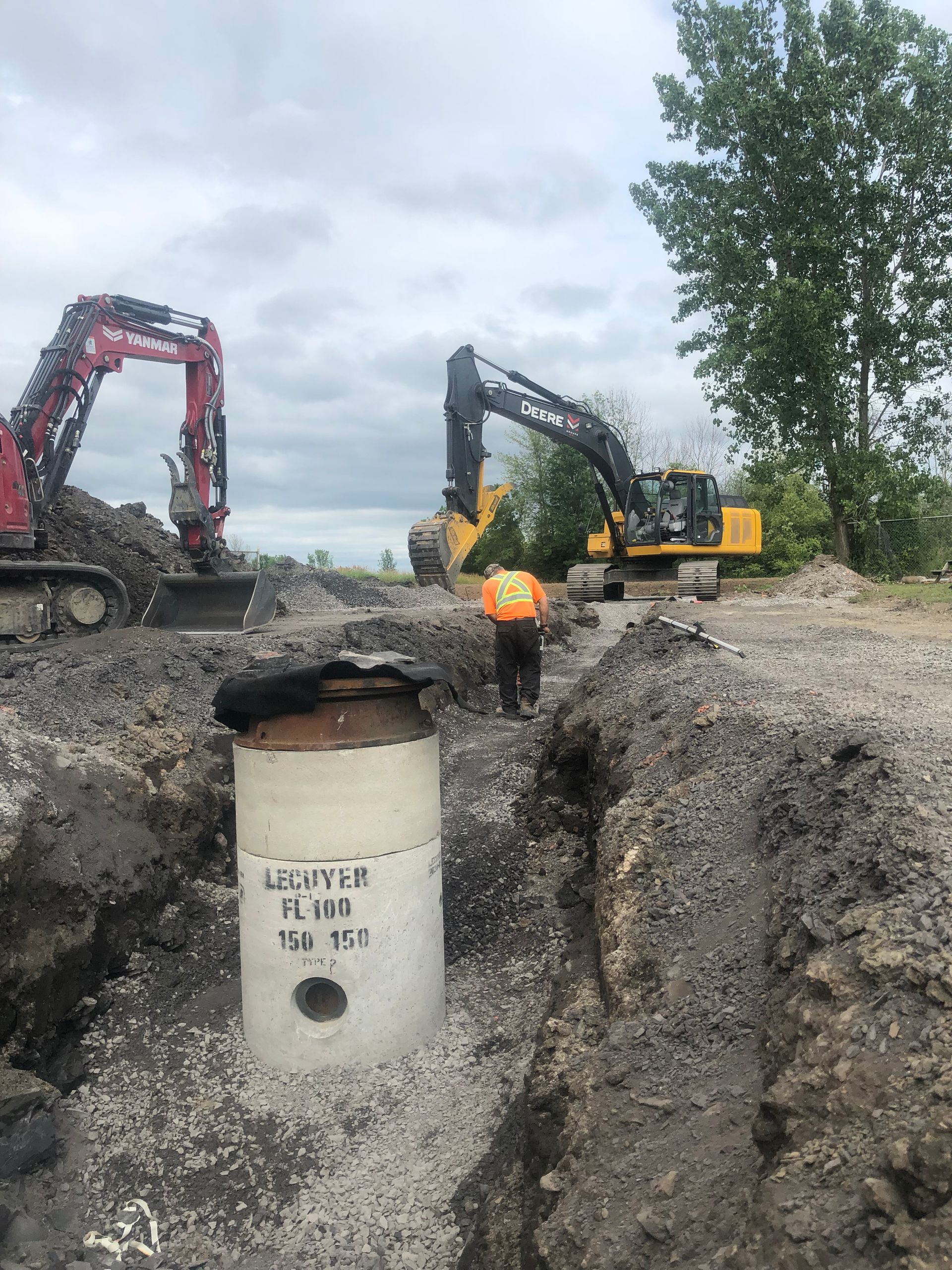 Un homme vêtu d'un gilet orange se tient à côté d'un tuyau dans la terre.
