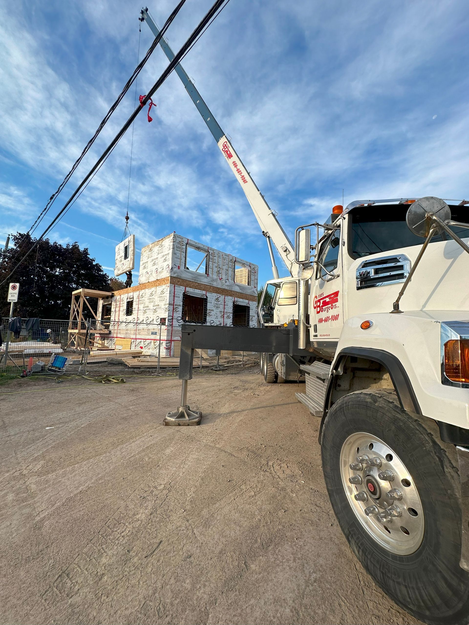Un camion blanc auquel est attachée une grue est garé devant un bâtiment en construction.