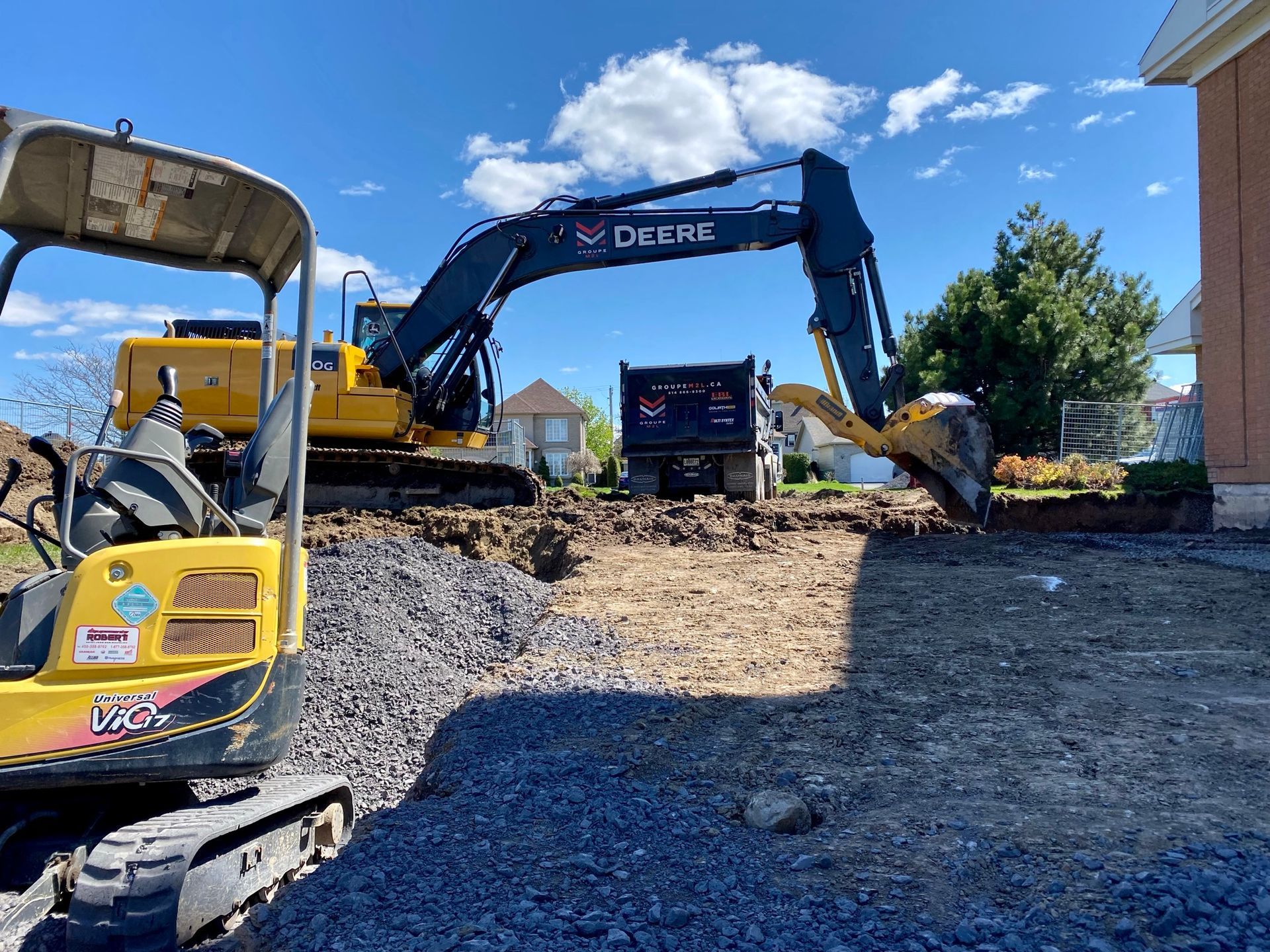 Une grande excavatrice creuse un trou dans la terre devant une maison.