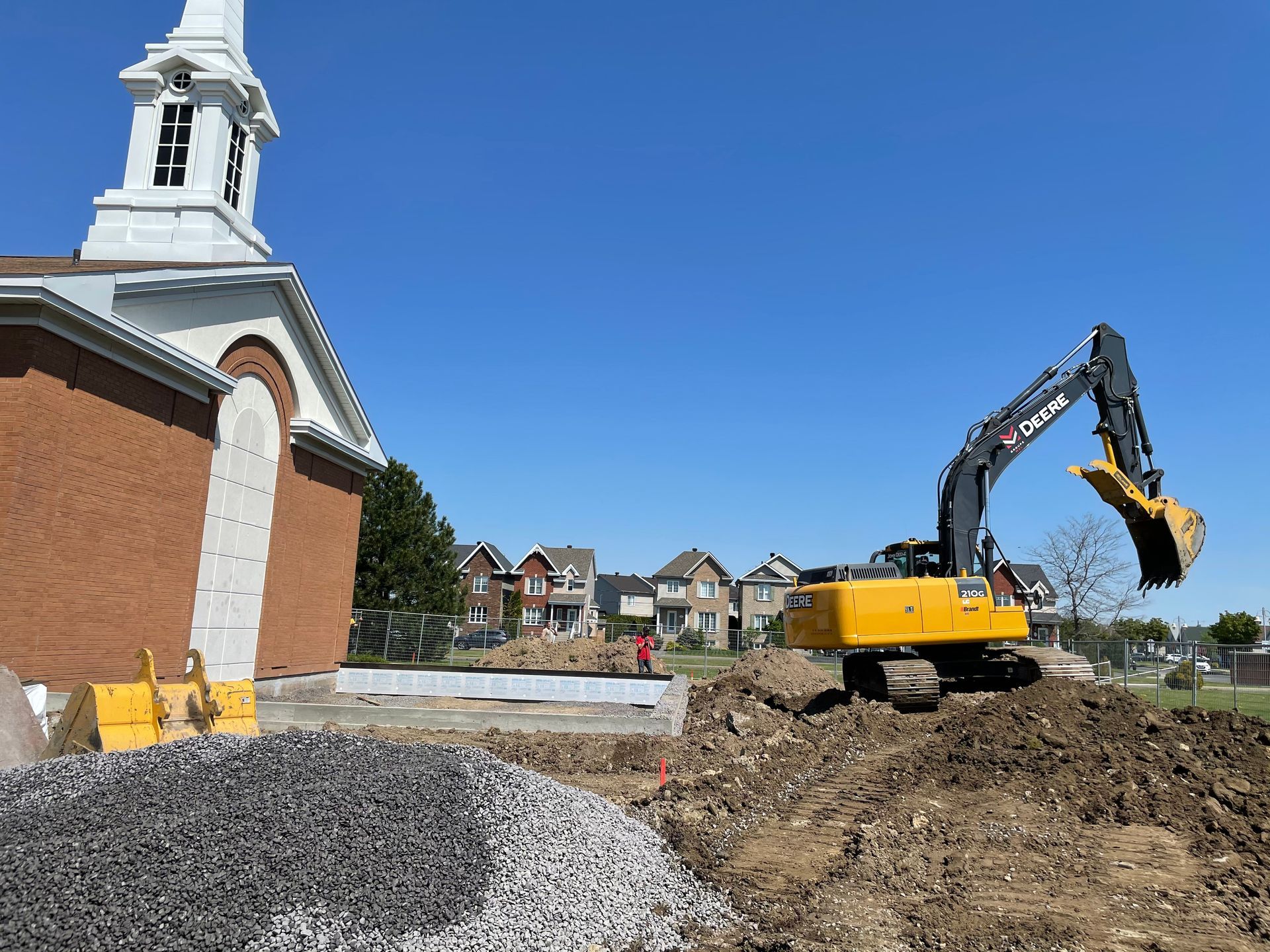 Une excavatrice jaune creuse un trou devant une église.