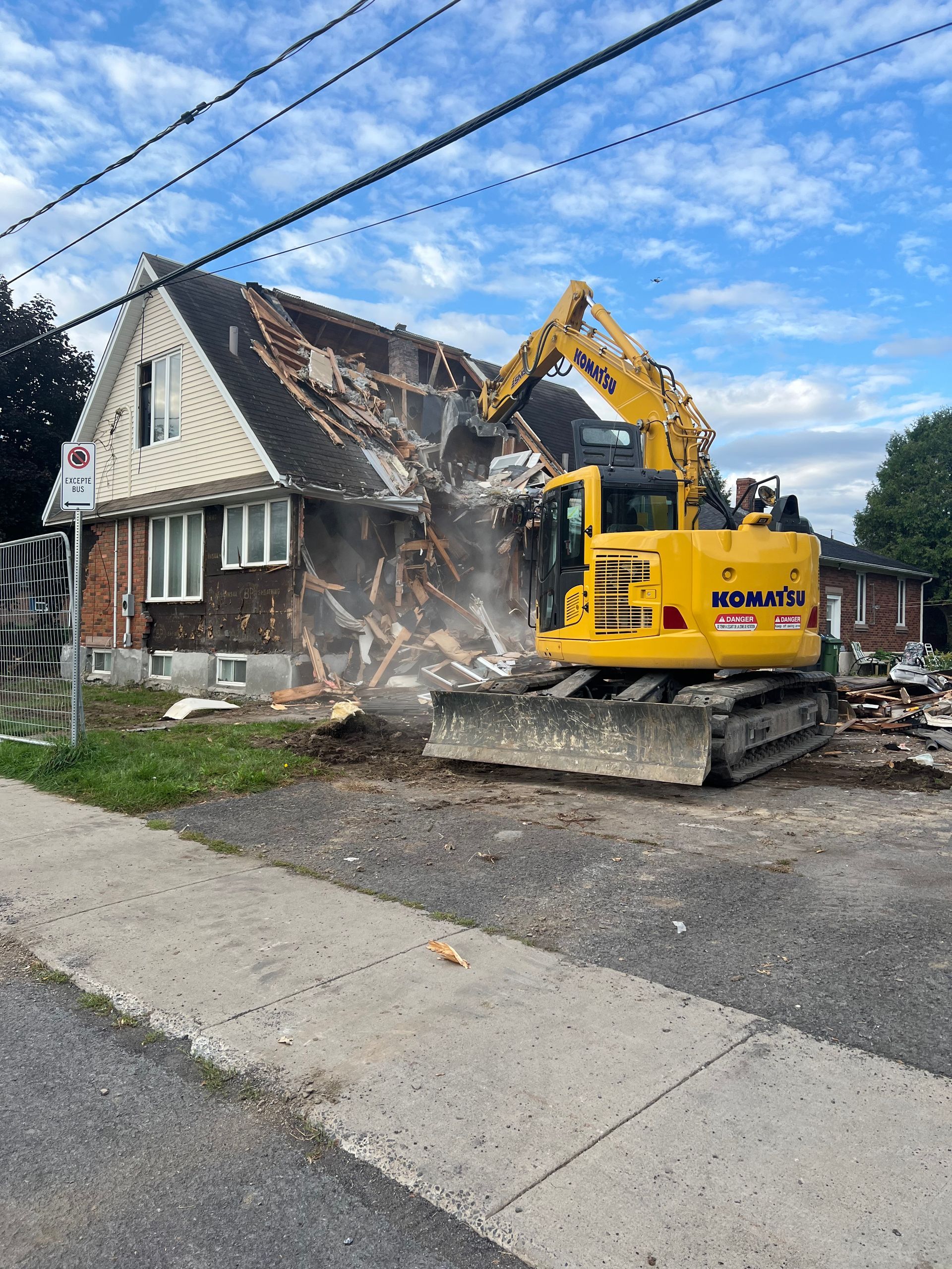Une pelle jaune est en train de démolir une maison au bord de la route.