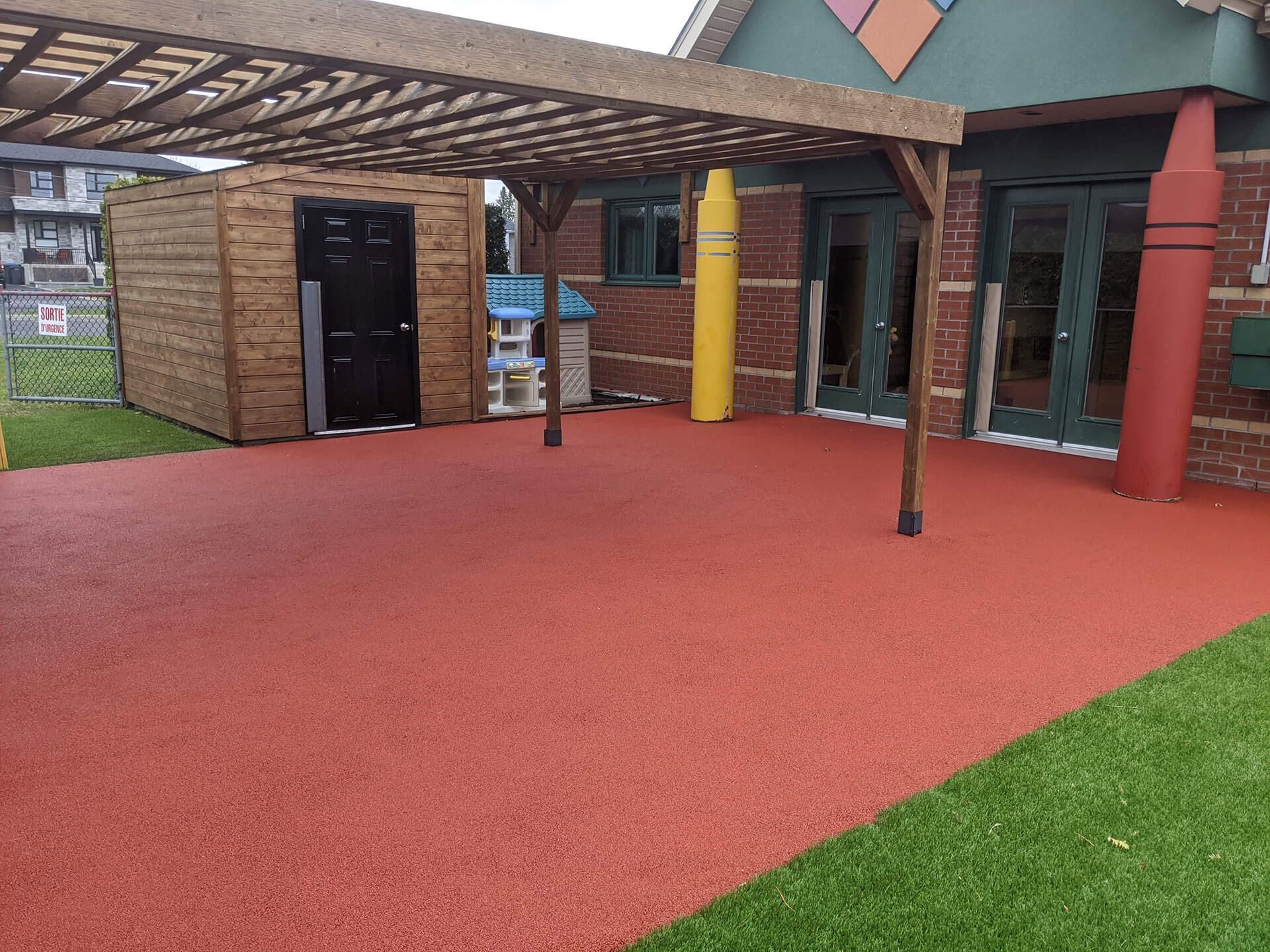 Un bâtiment en brique avec un sol rouge et un hangar en bois.