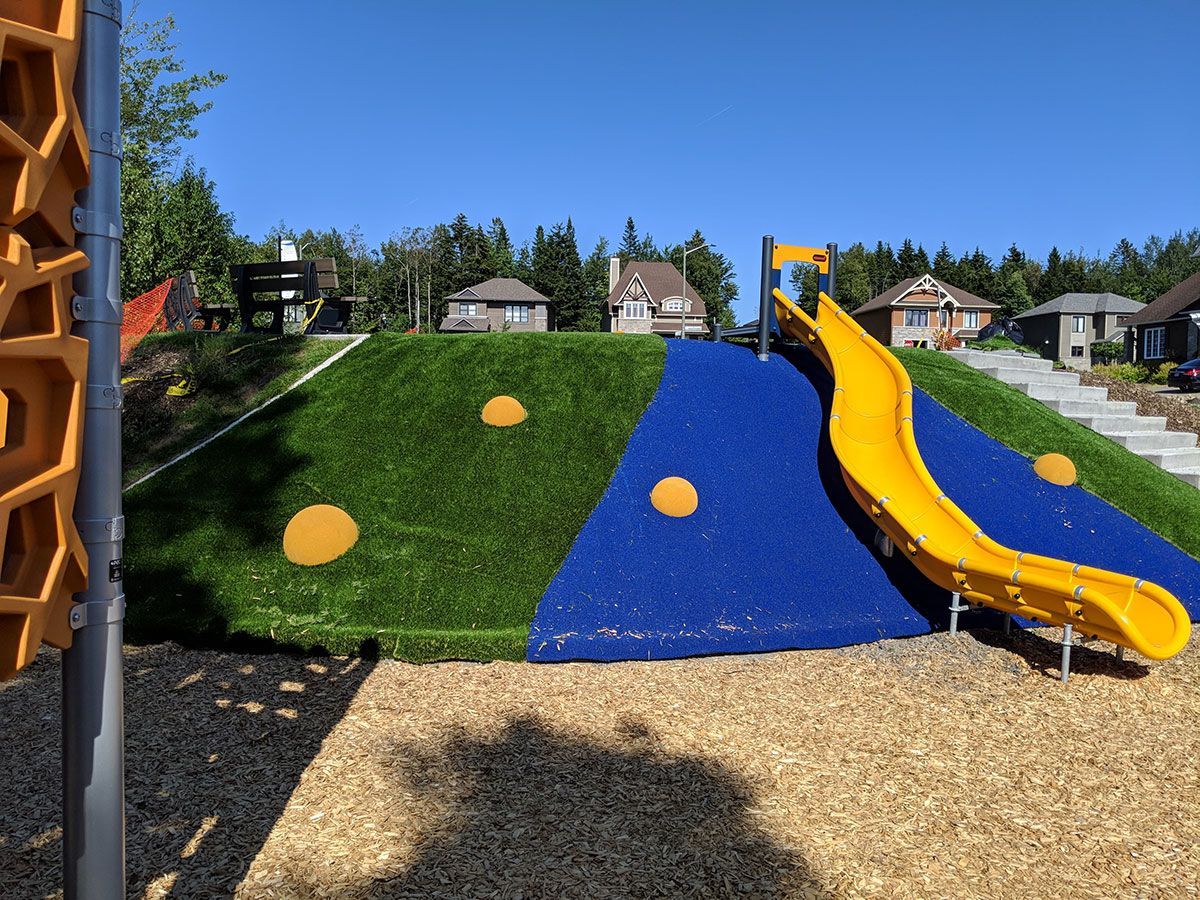 Un toboggan jaune descend une colline dans un terrain de jeu.