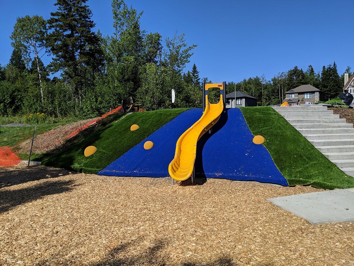 Un toboggan jaune se trouve au sommet d'une colline bleue dans une aire de jeux.