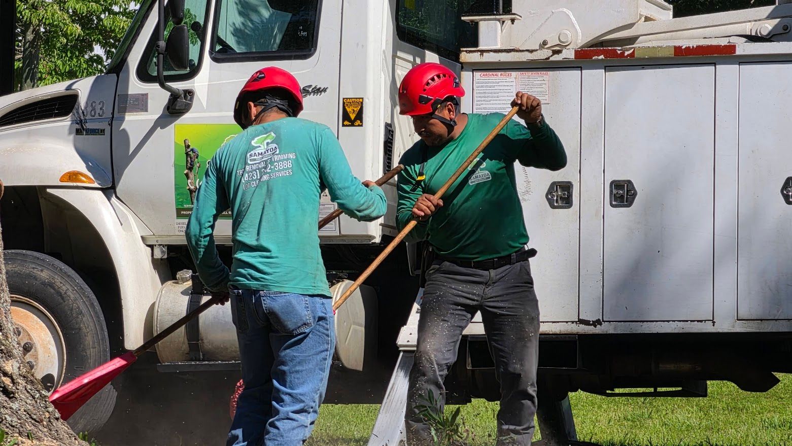 Workers loading debris into a white dump truck on a suburban street with a yellow loader nearby