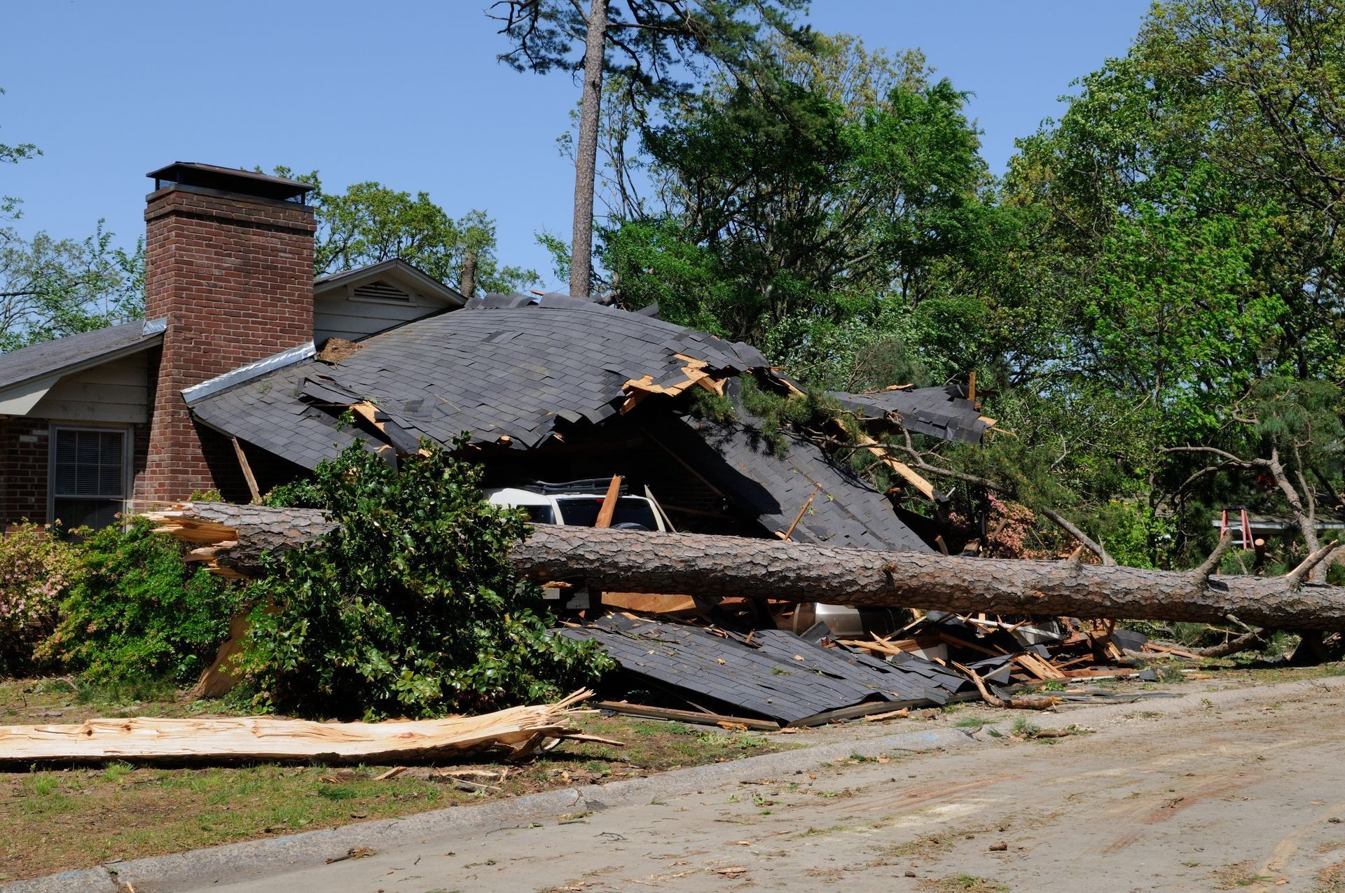 Collapsed house with fallen roof and chimney, damaged by storm, beside a street and trees