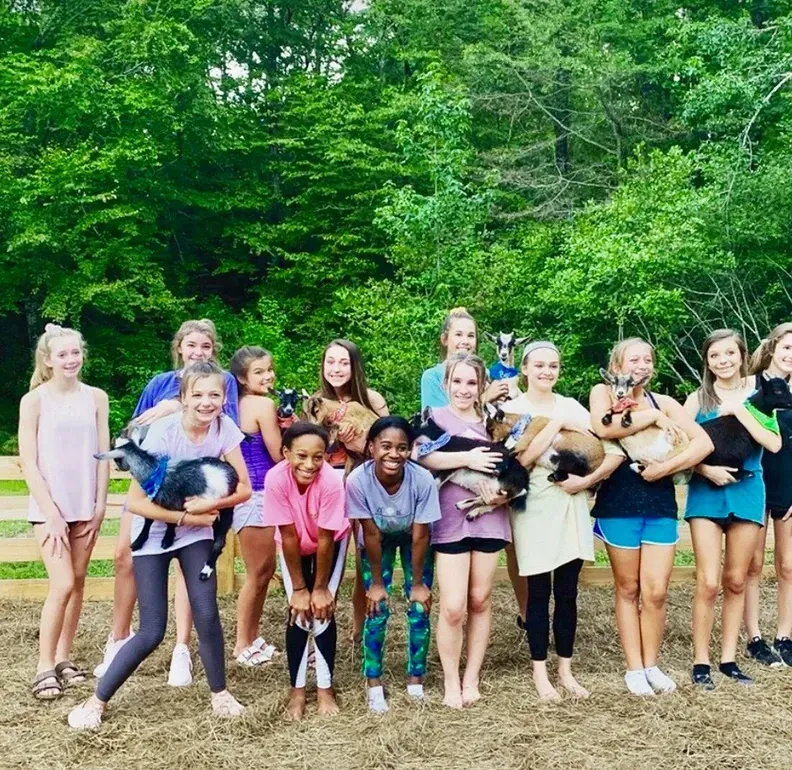 A group of young girls are posing for a picture while holding goats.