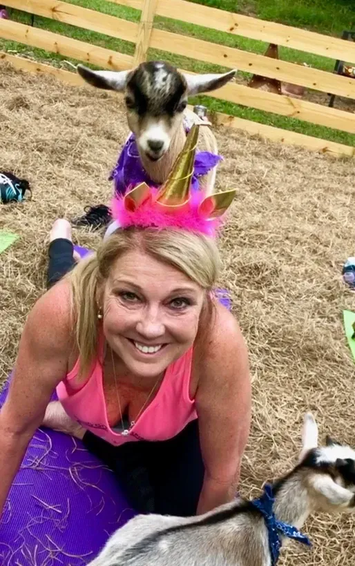 A woman is sitting on a yoga mat next to two goats.