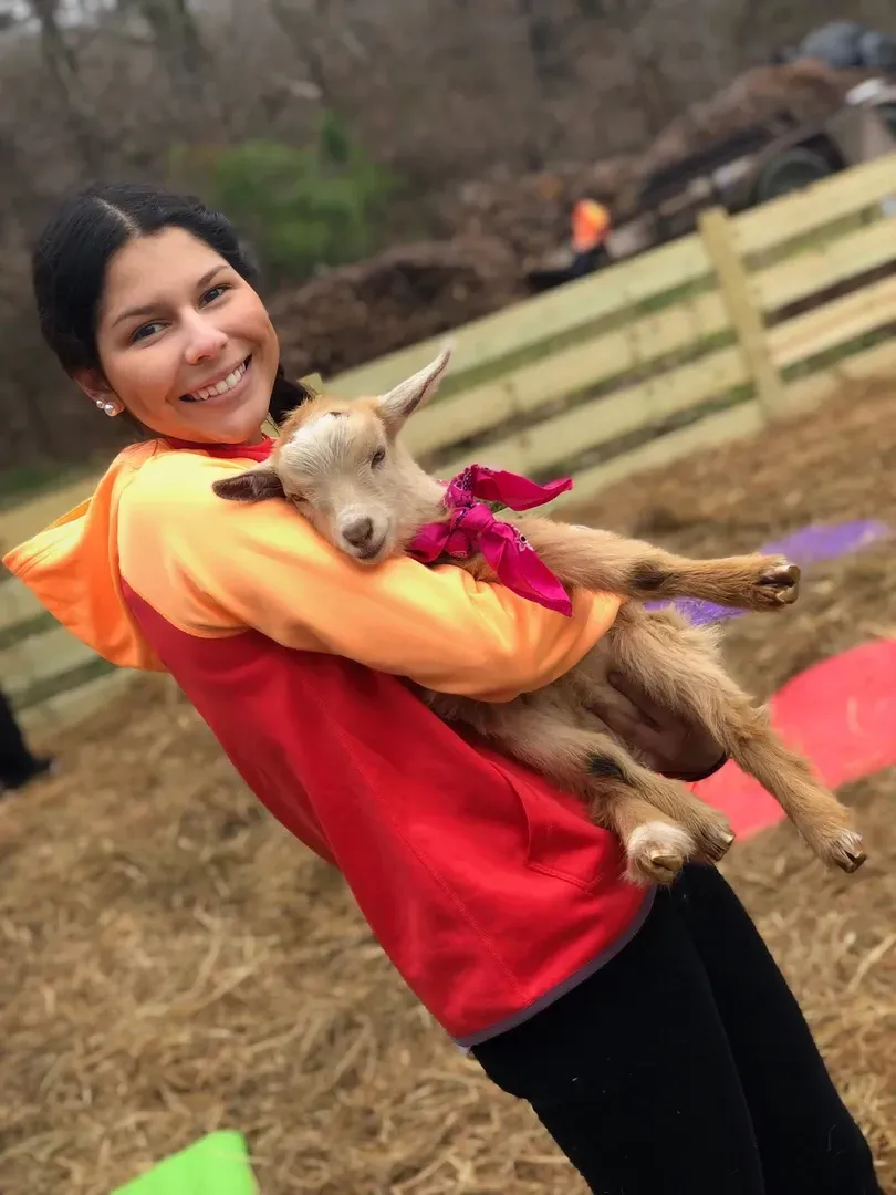 A woman is holding a baby goat in her arms.