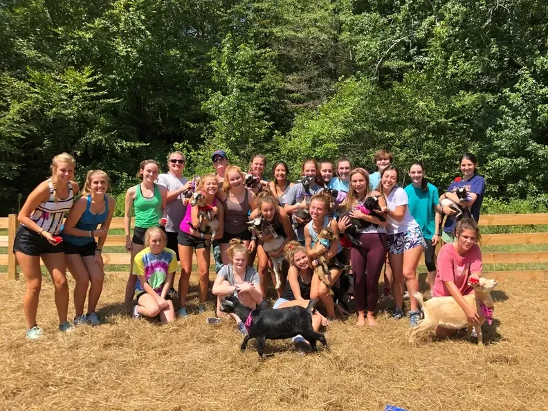 A group of young girls are posing for a picture with a goat.