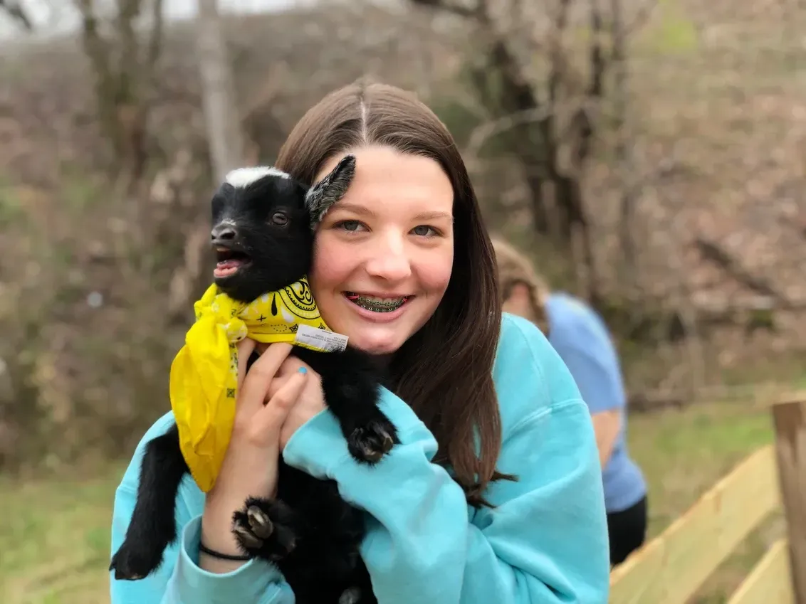 A girl is holding a baby goat in her arms.