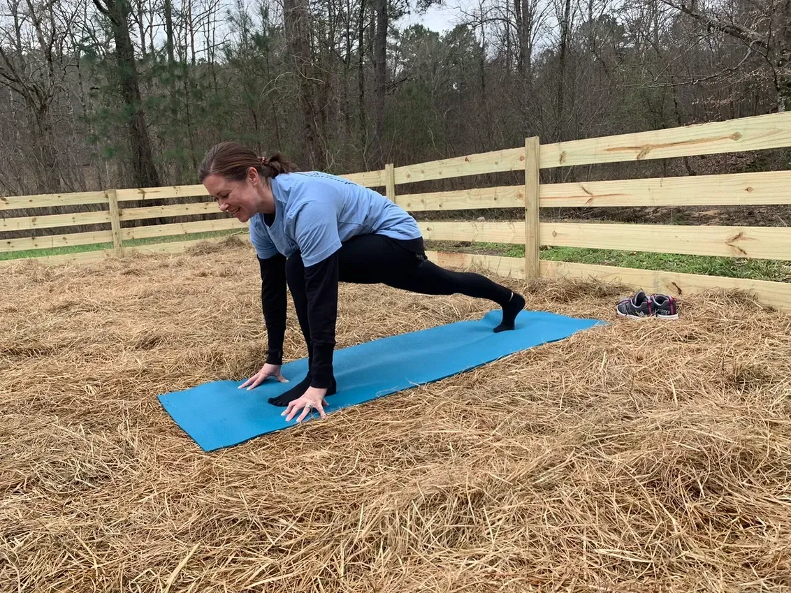 A woman is doing a yoga pose on a blue mat in a field.