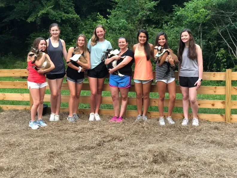 A group of girls are standing next to each other holding puppies in front of a wooden fence.