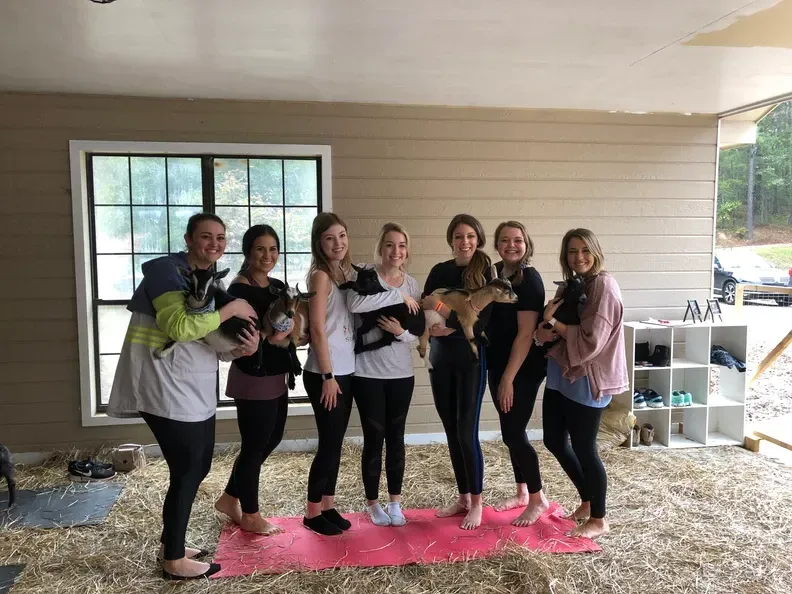 A group of women are standing next to each other on a yoga mat holding puppies.