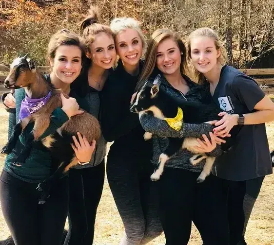 A group of women are posing for a picture while holding goats