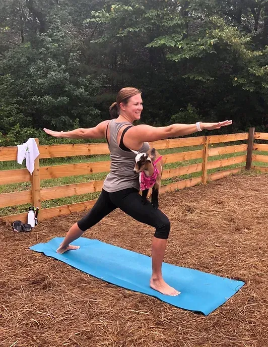 A woman is practicing yoga with a dog in her arms.