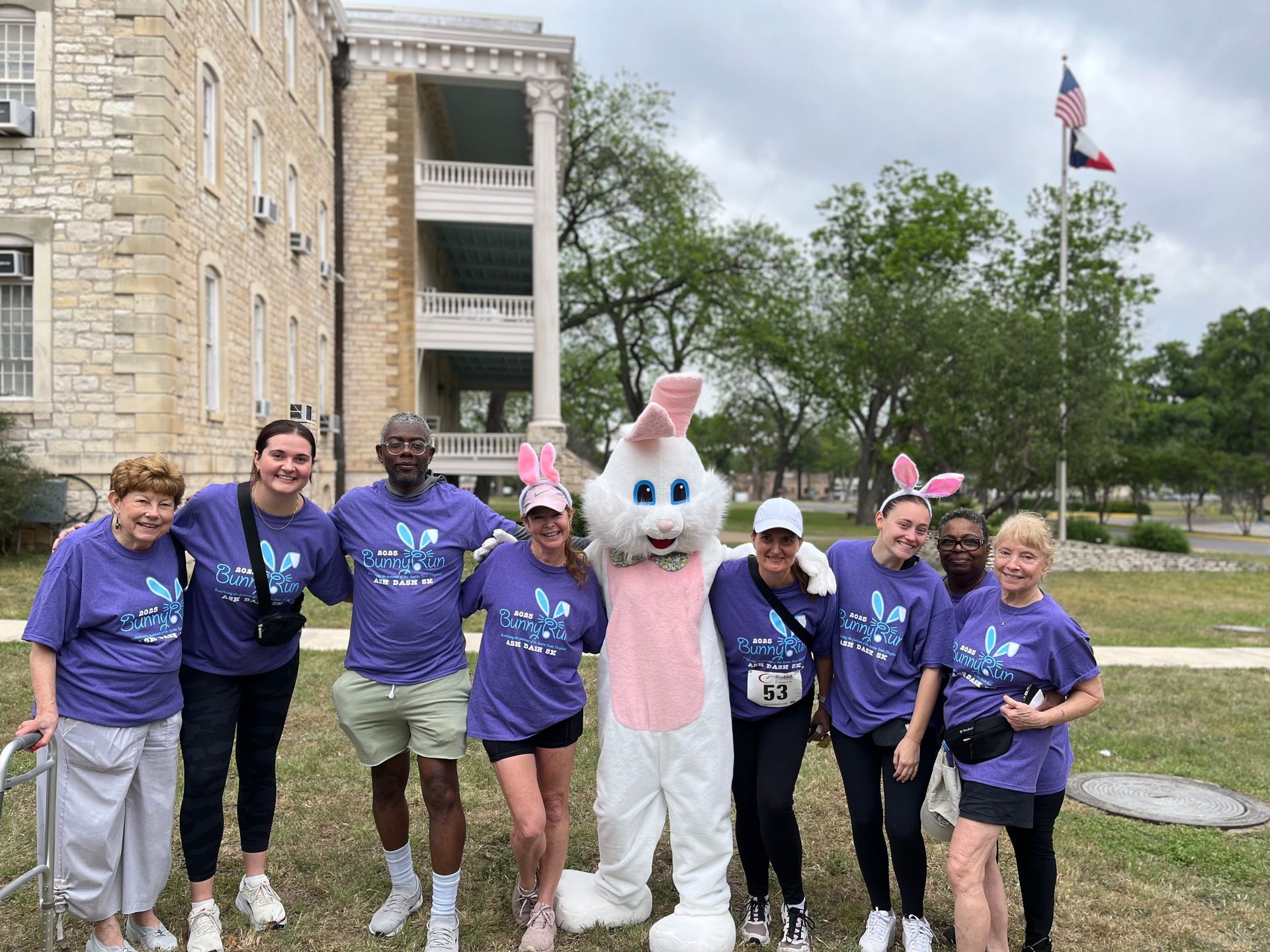 Group of people pose with Easter Bunny in front of building; all wearing purple shirts.