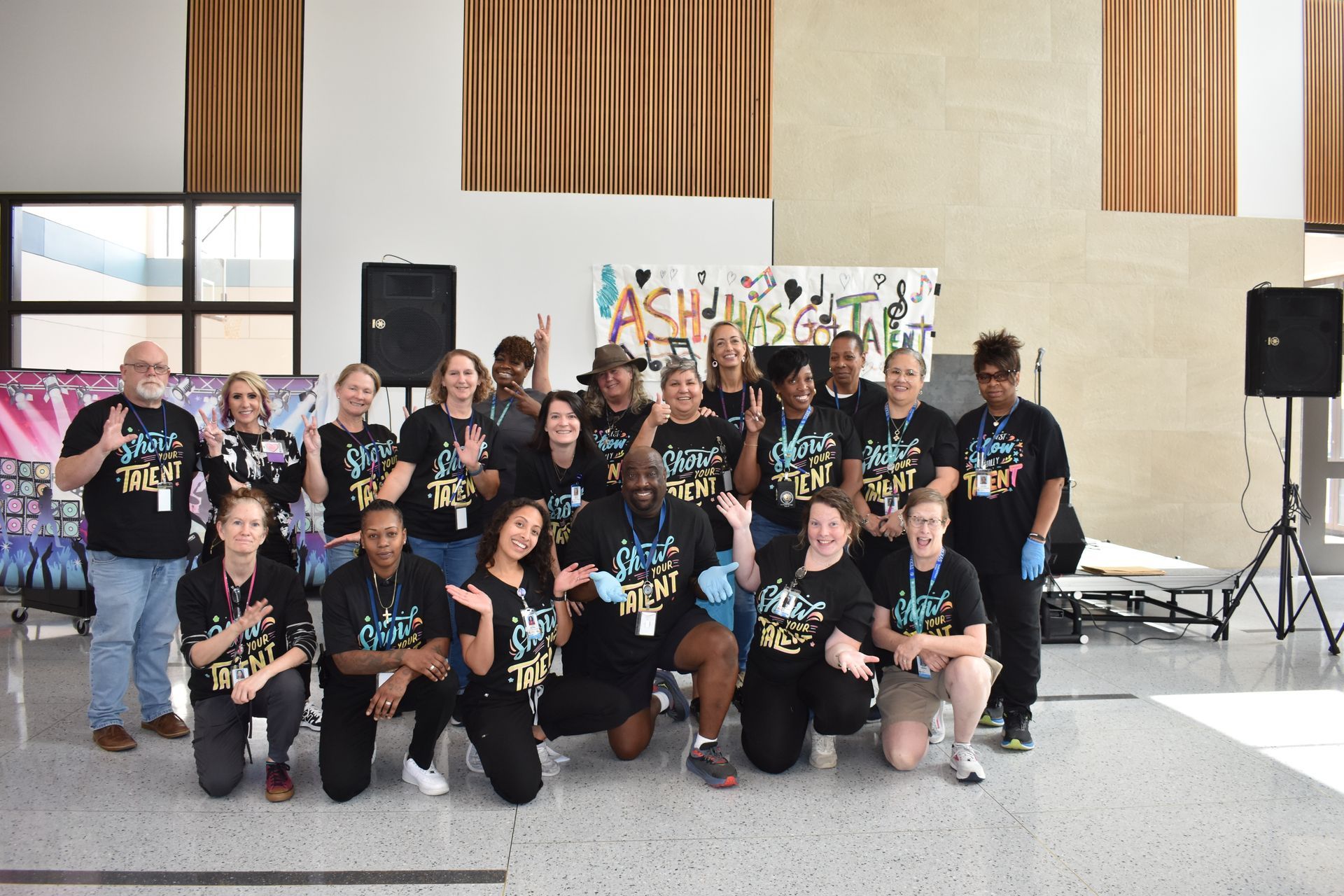Group of people in matching black shirts posing outdoors in front of a building and banner