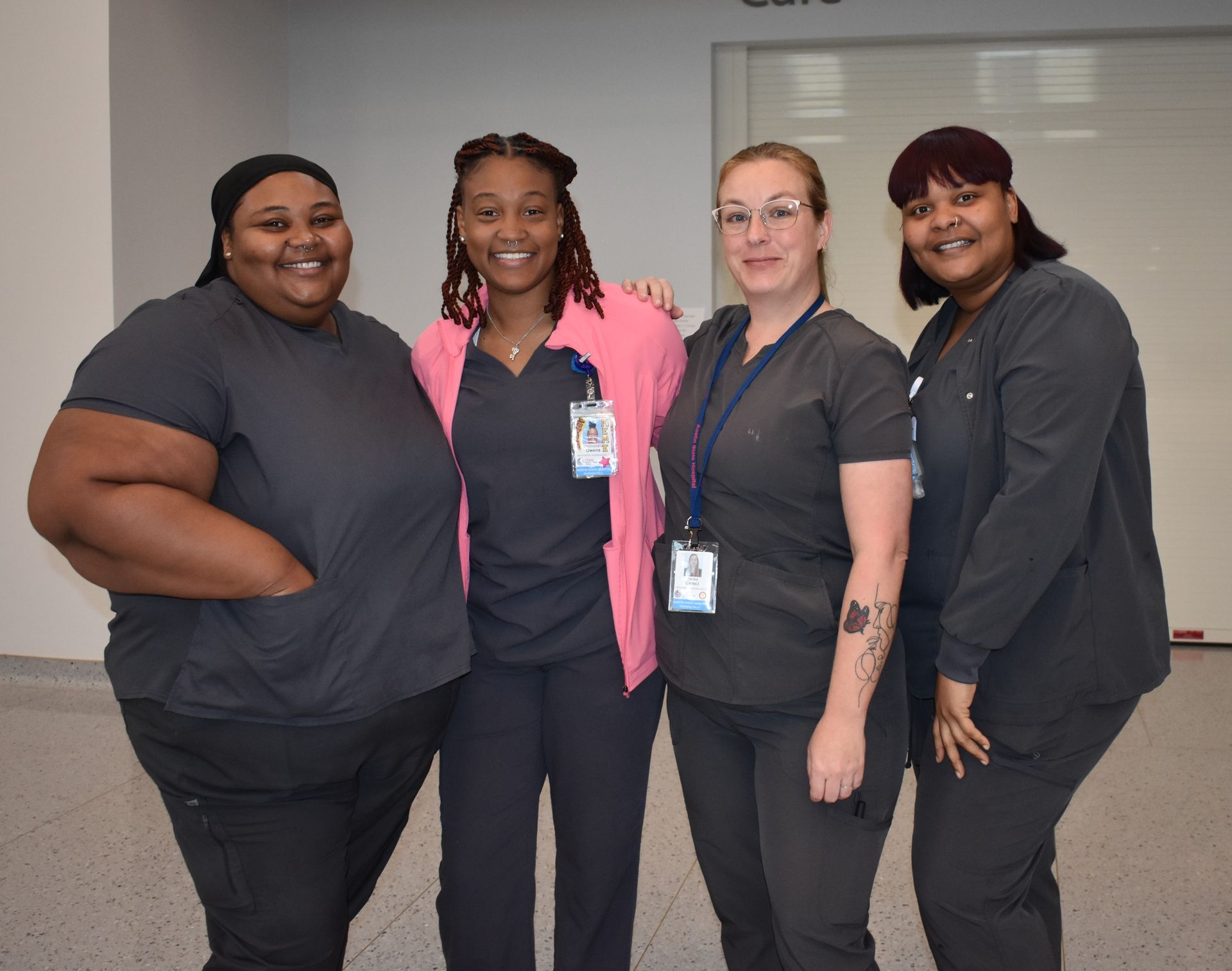 Four coworkers standing together indoors, smiling in dark uniforms with ID badges.