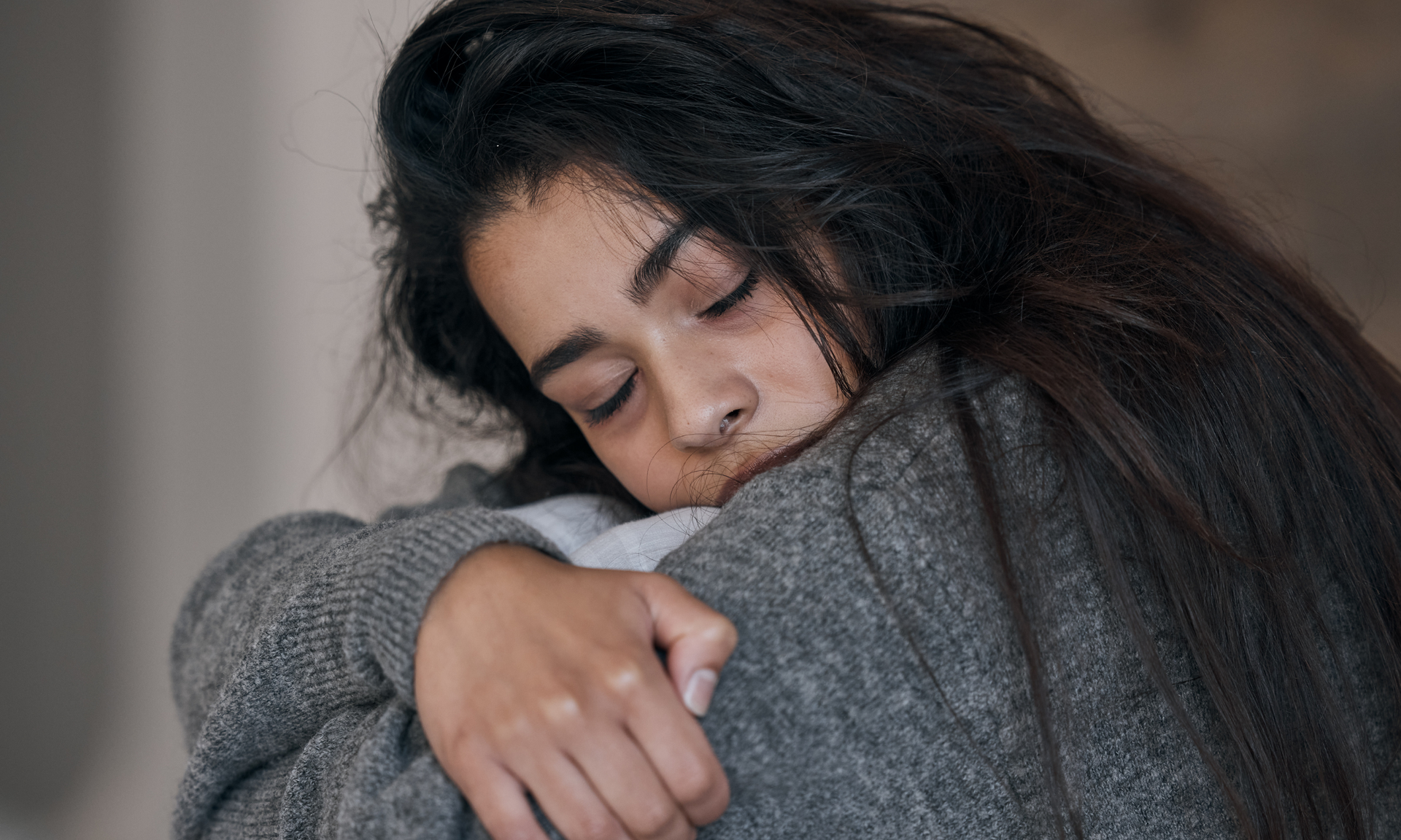 Woman in gray sweater, hugging herself, with eyes closed.