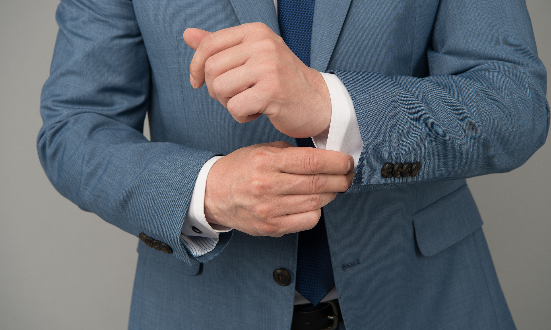 Man adjusting light blue suit cuff with white shirt sleeve.