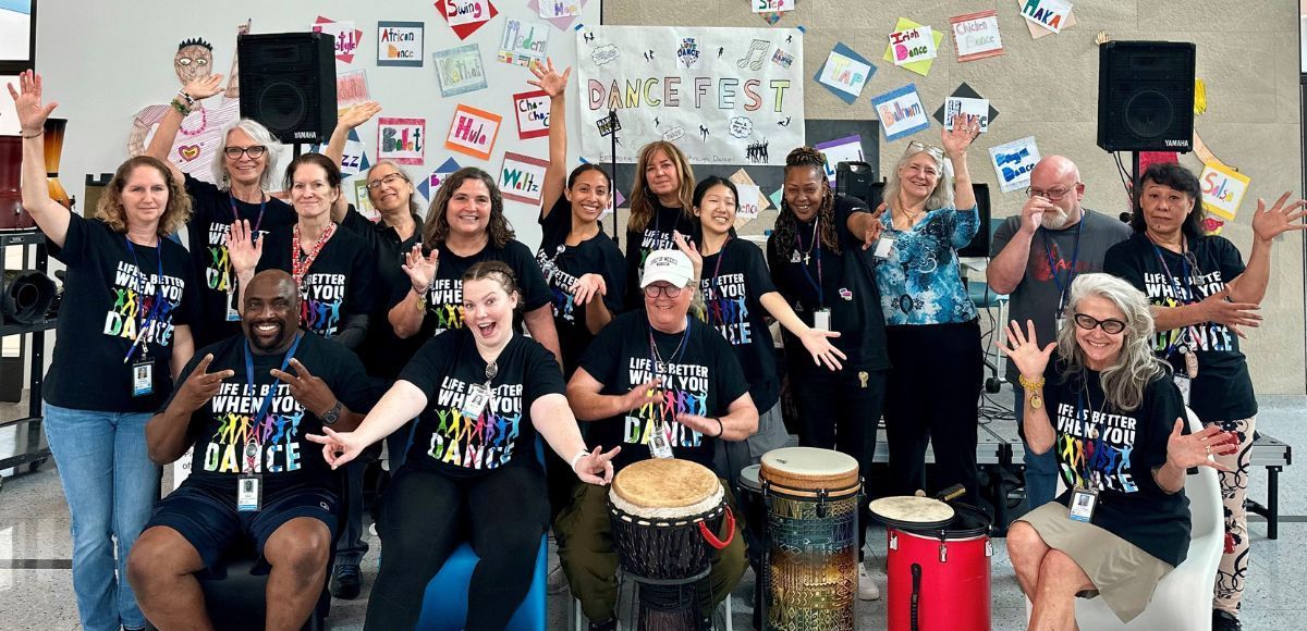 Group of people posing with drums and painted signs in front of a colorful mural wall