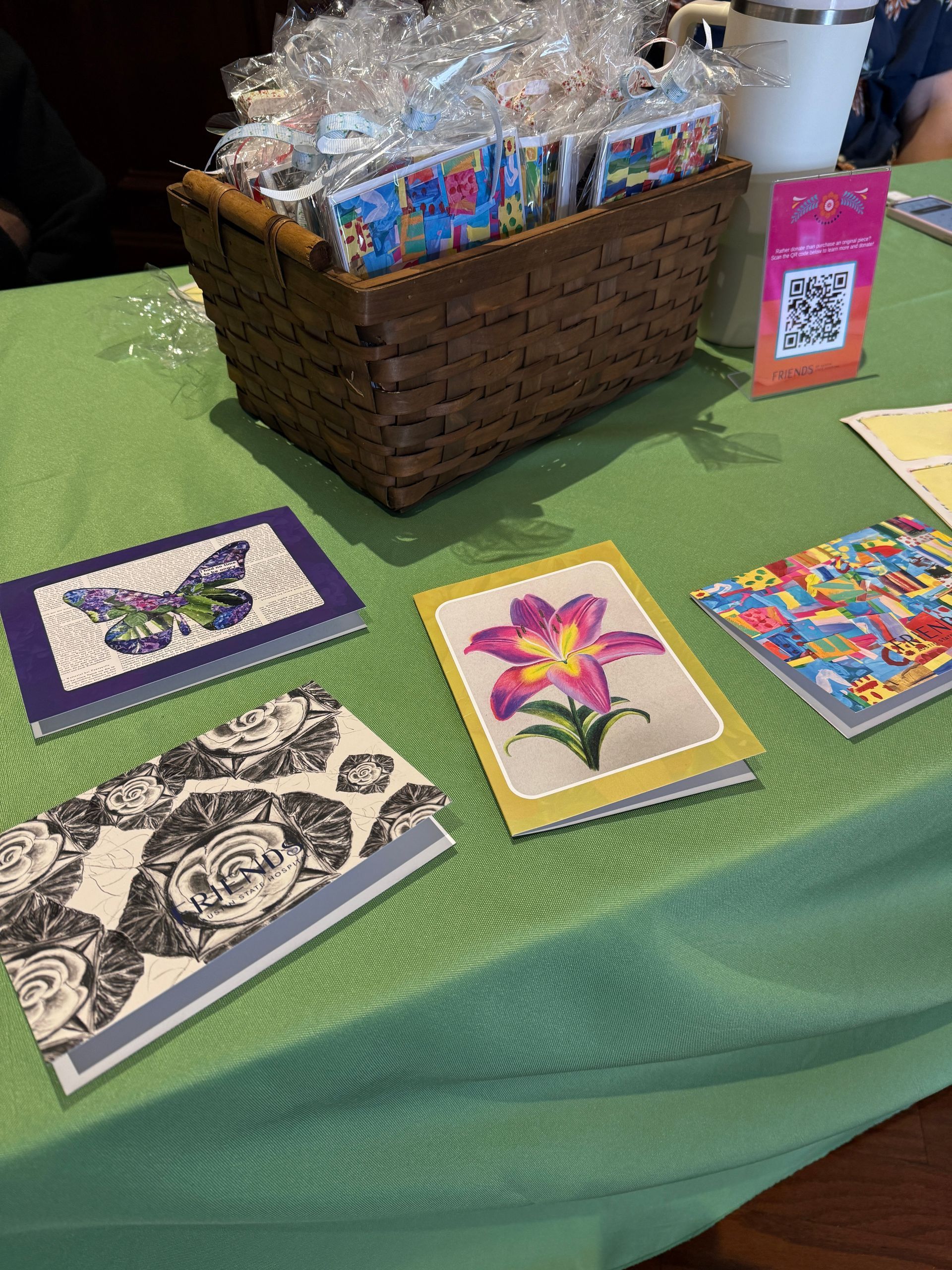 A woven basket of wrapped cards sits on a green tablecloth next to several cards featuring butterfly, floral, and art designs.